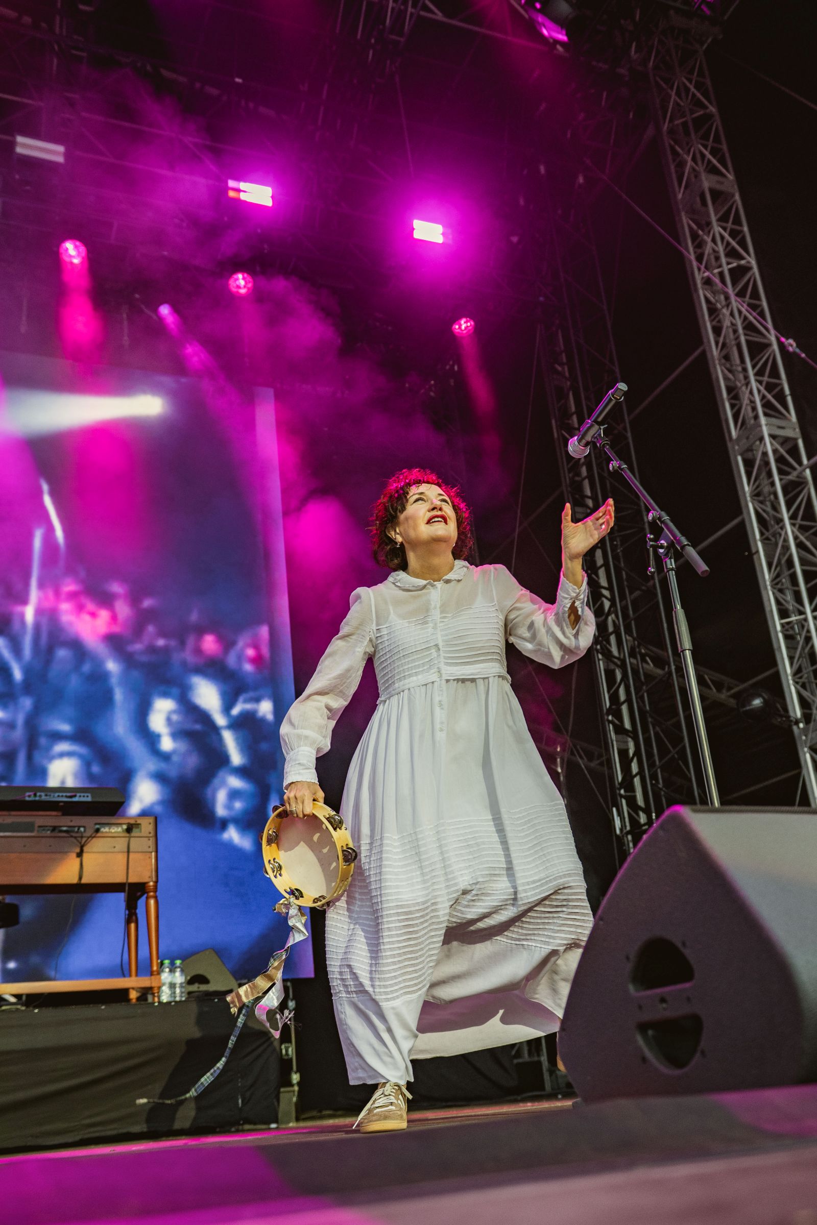 Performer in white dress with tambourine on stage with pink lights