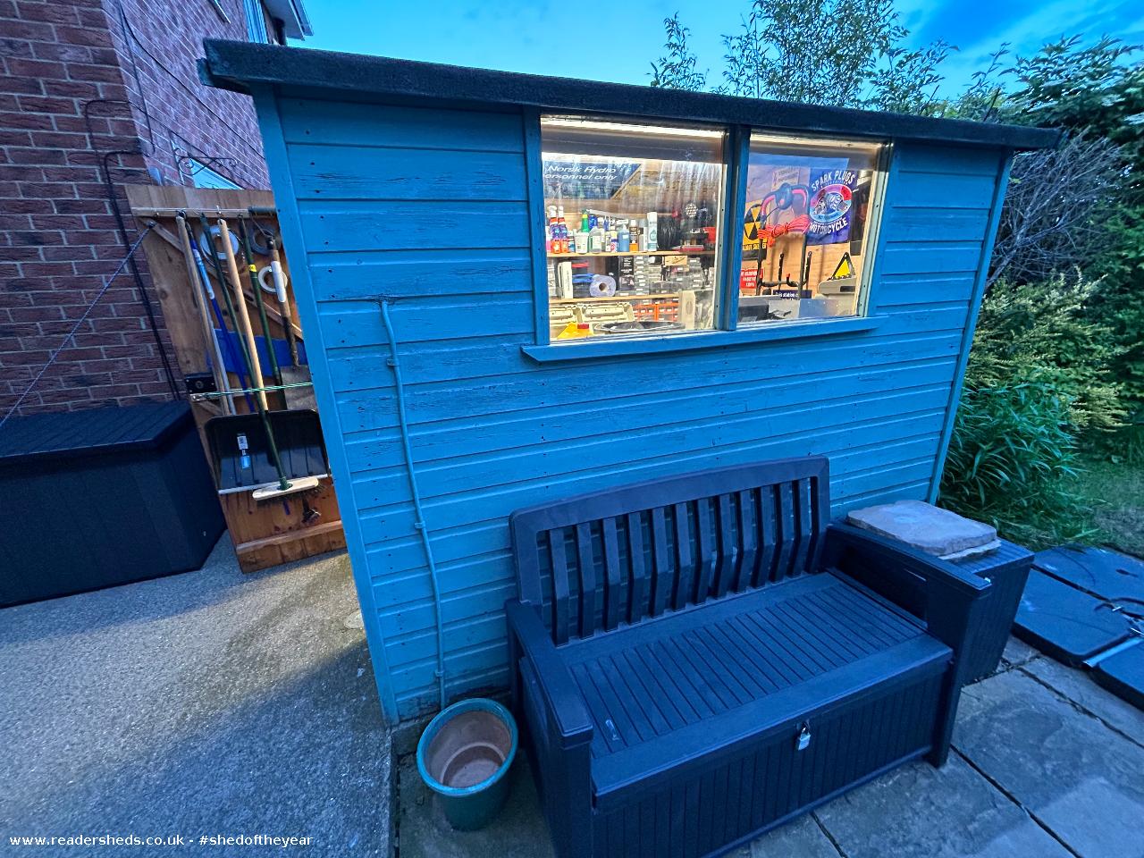 Blue wooden garden shed with large window and outdoor seating