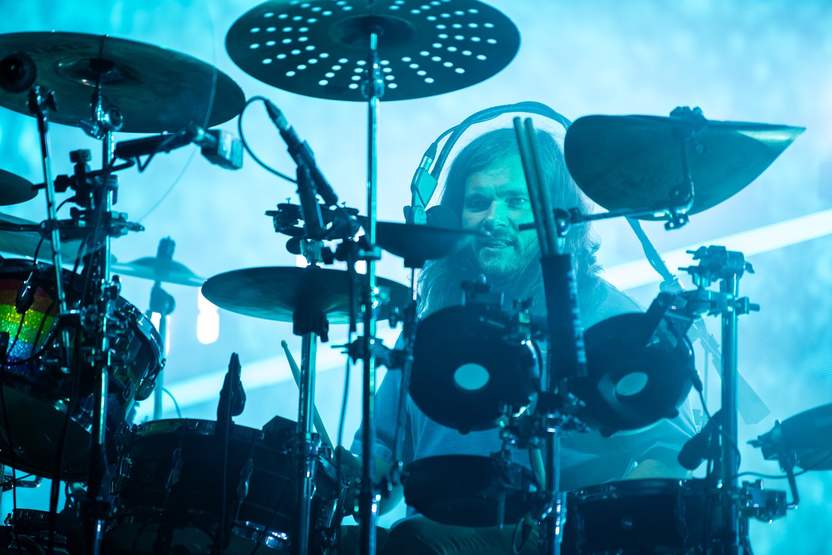 Drummer playing a complex drum kit under blue stage lights