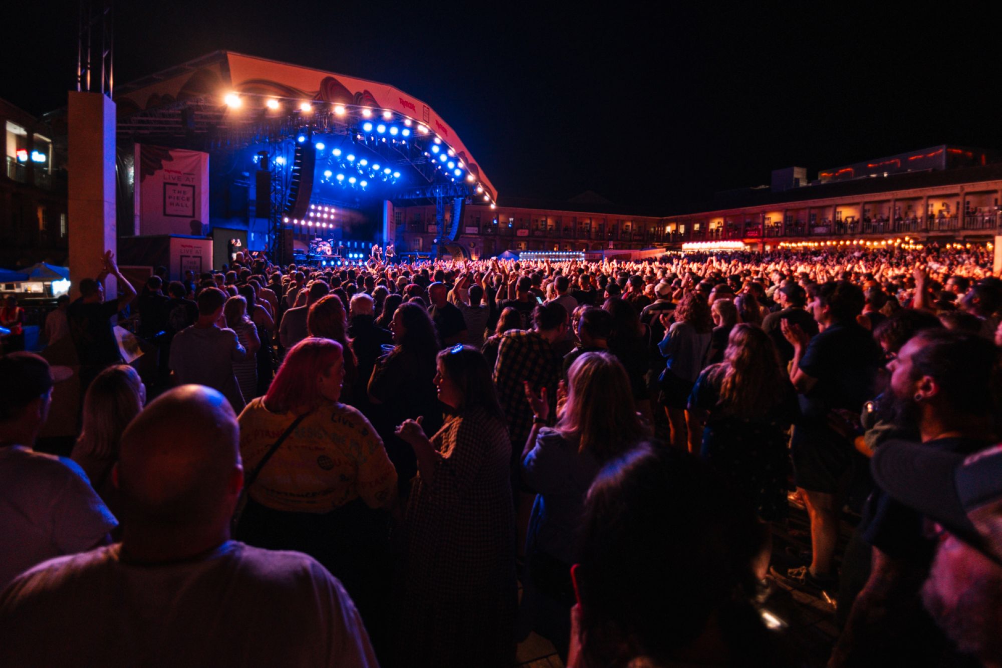 Crowd enjoying an outdoor nighttime concert with bright stage lights