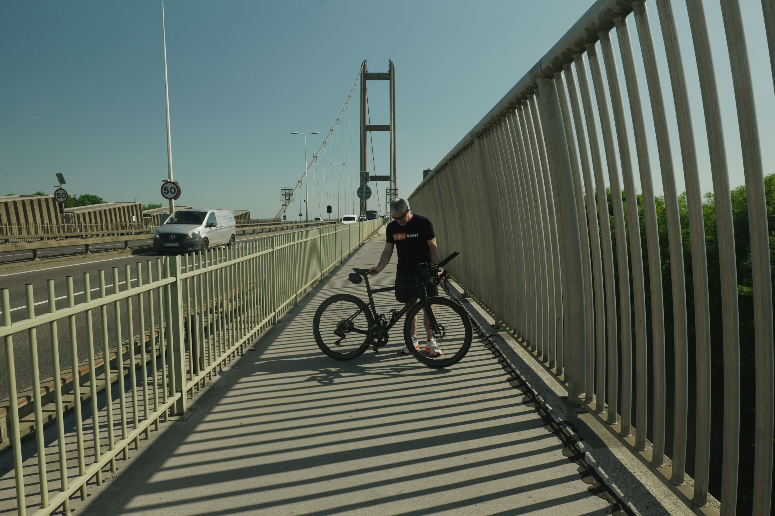 Cyclist resting on Humber Bridge footpath with shadows