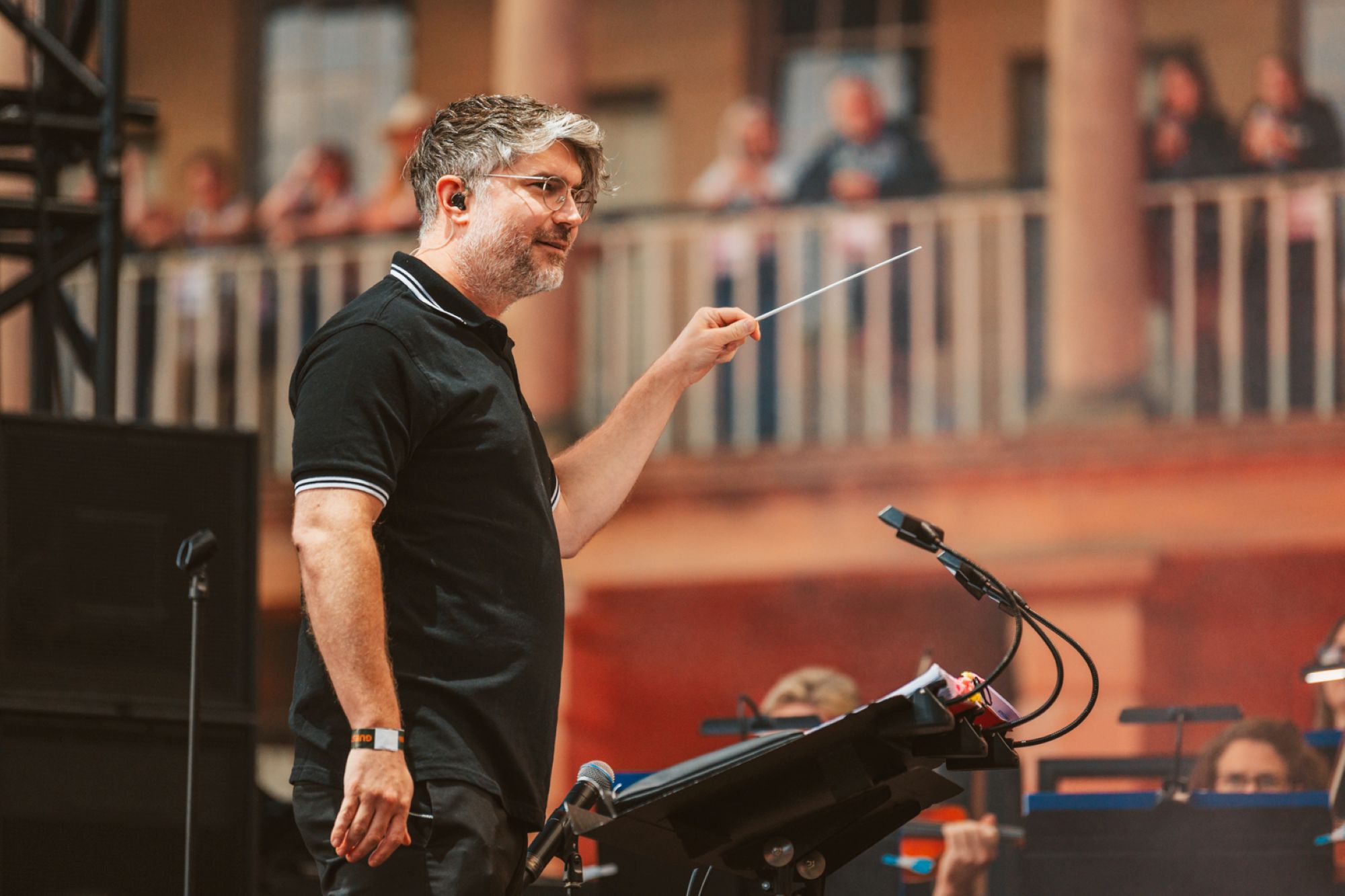 Conductor leading an outdoor orchestra with historic building backdrop
