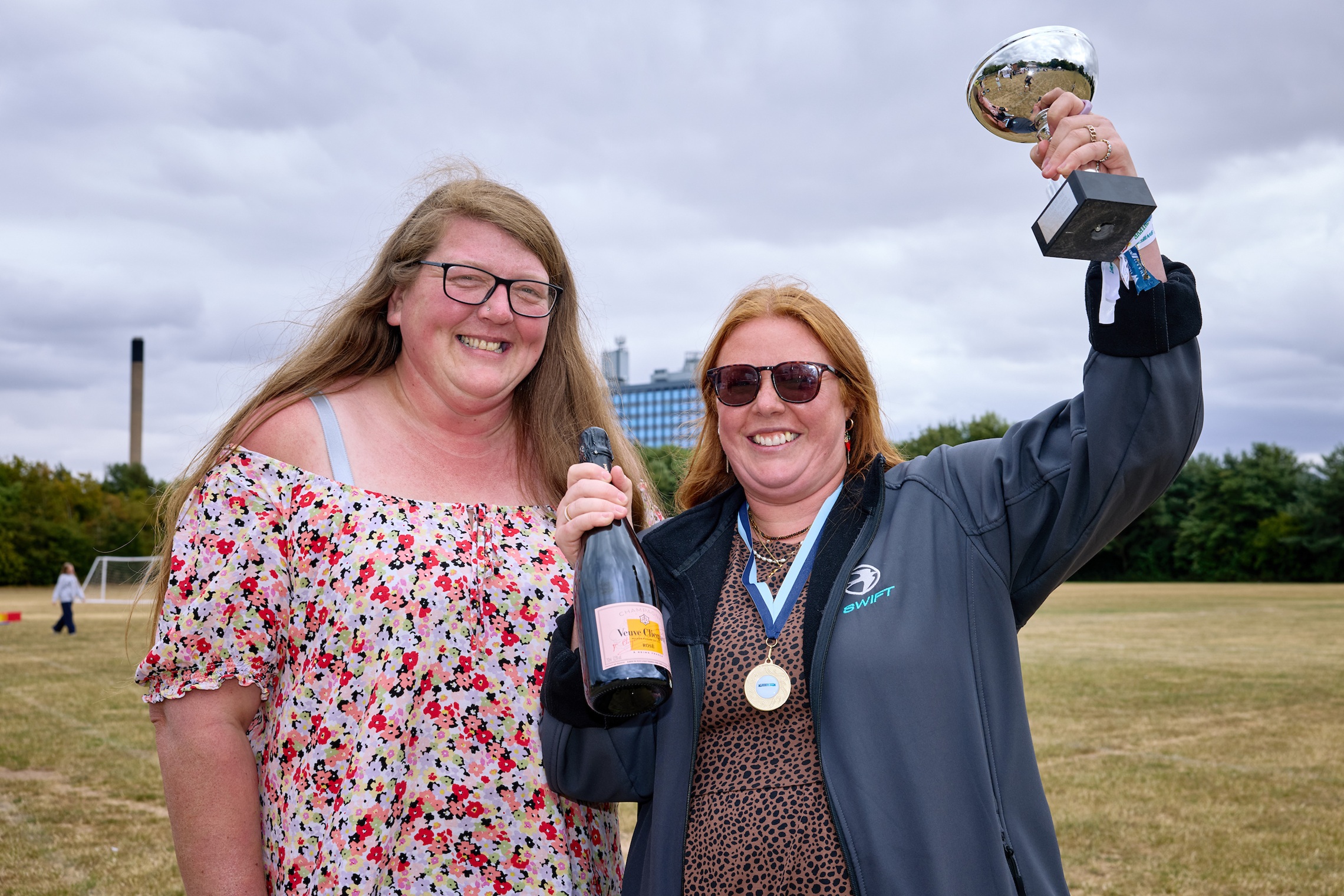 Two women celebrating with a trophy and champagne outdoors