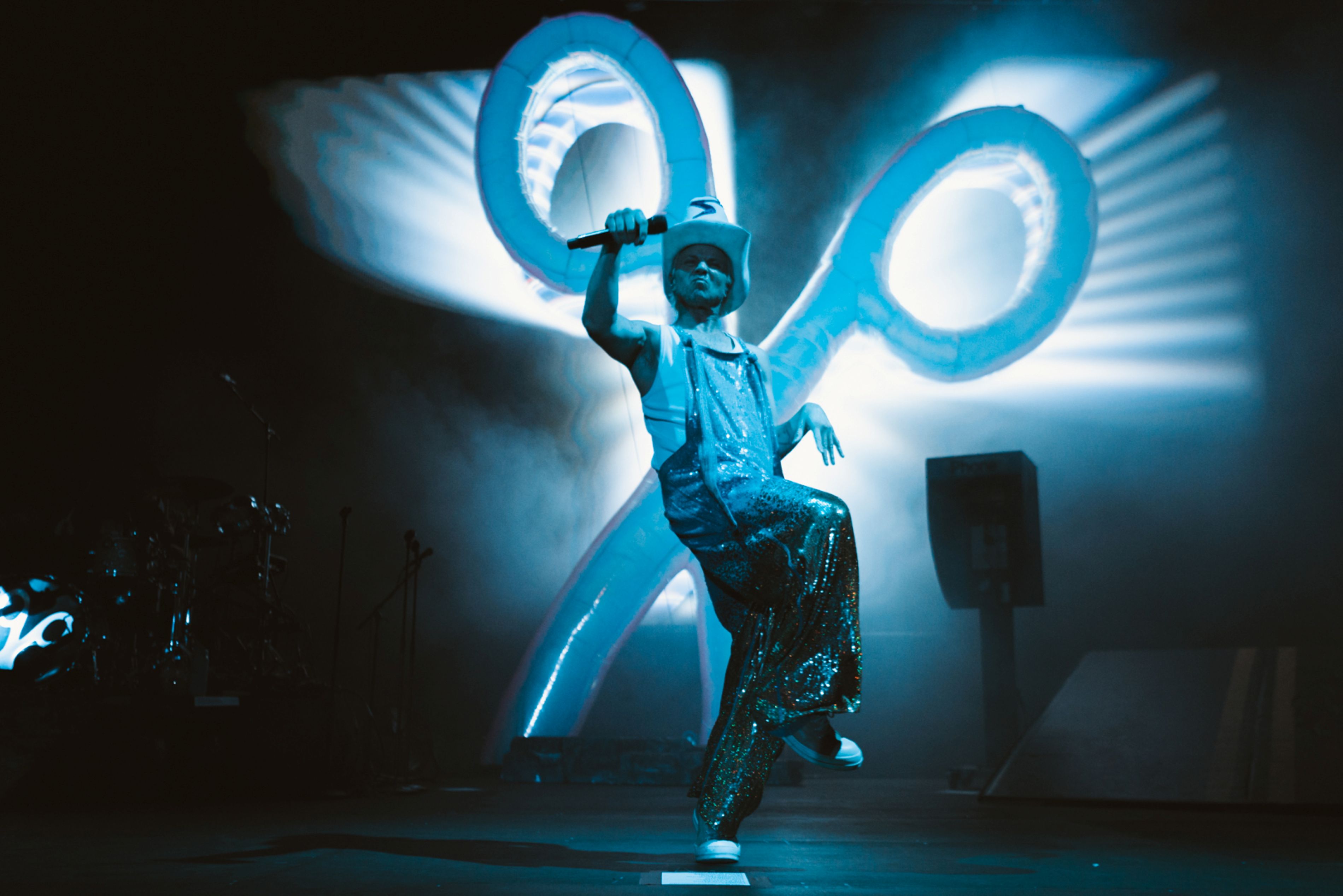 Lively performer in sequin trousers on stage with giant scissors backdrop