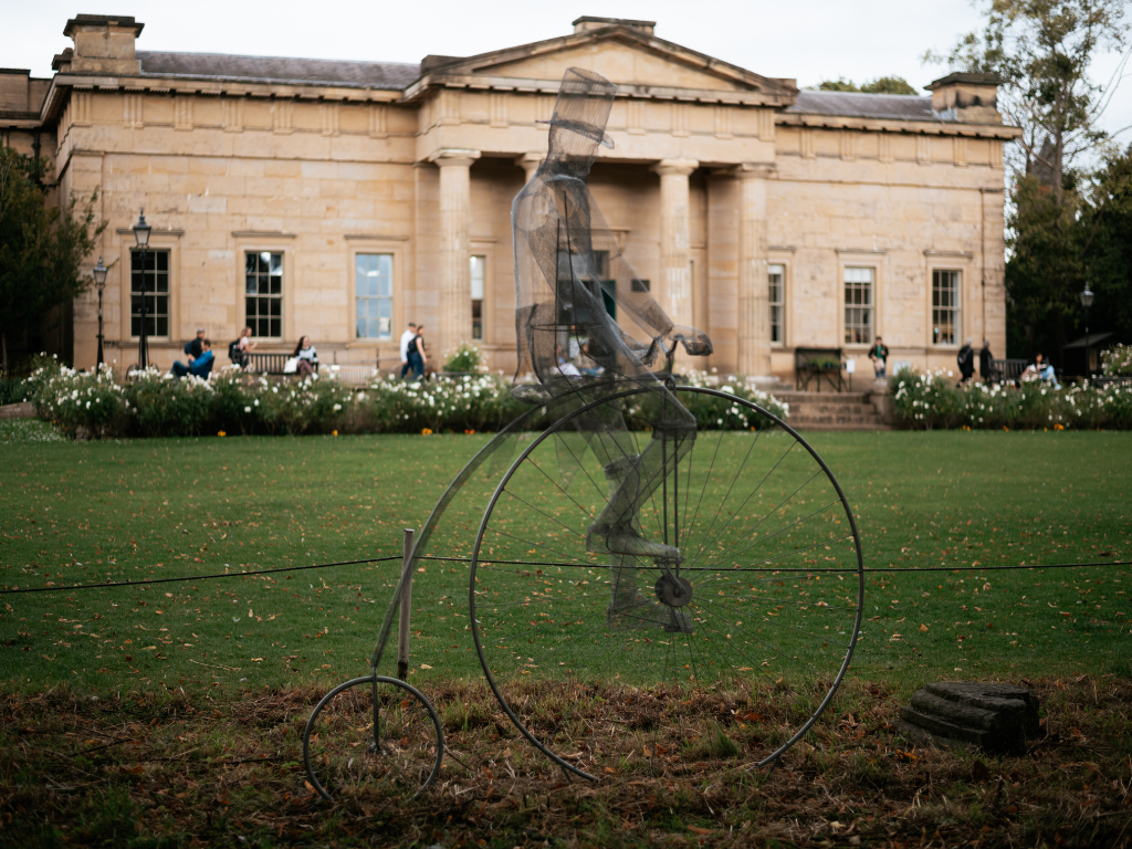 Historic stone building with a penny-farthing sculpture in the foreground