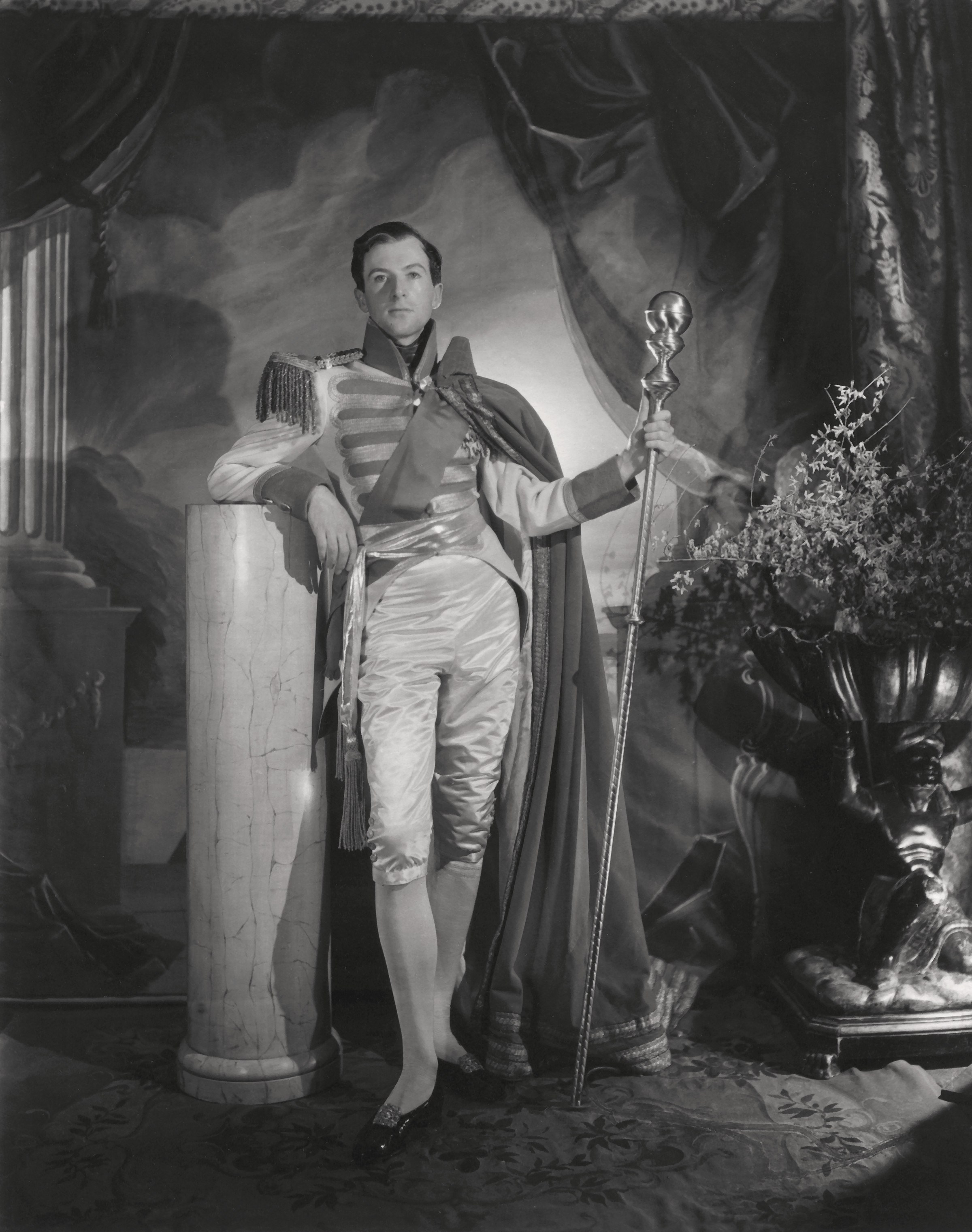 Man in historical costume with sceptre beside marble column