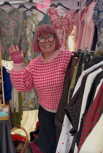 Smiling woman with pink hair in a market stall with clothes