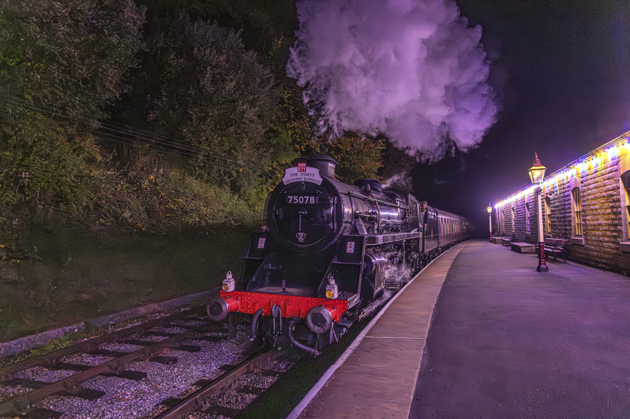 Steam locomotive at night with illuminated platform lights
