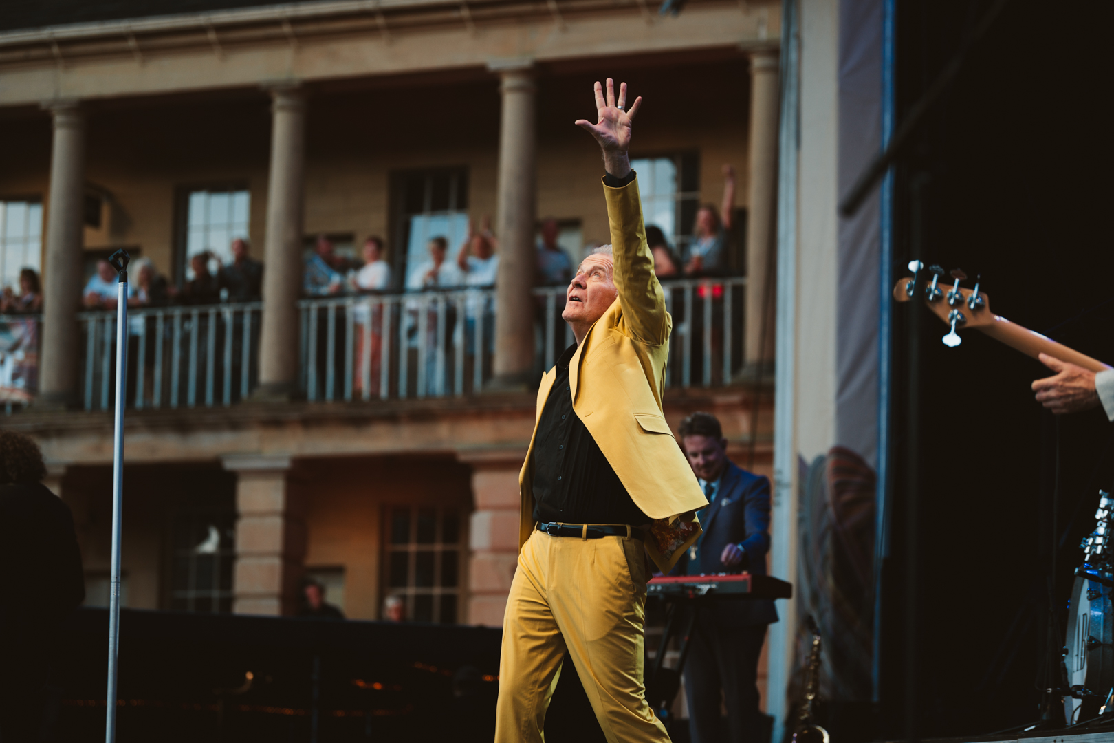 Performer in yellow suit on outdoor stage with cheering crowd