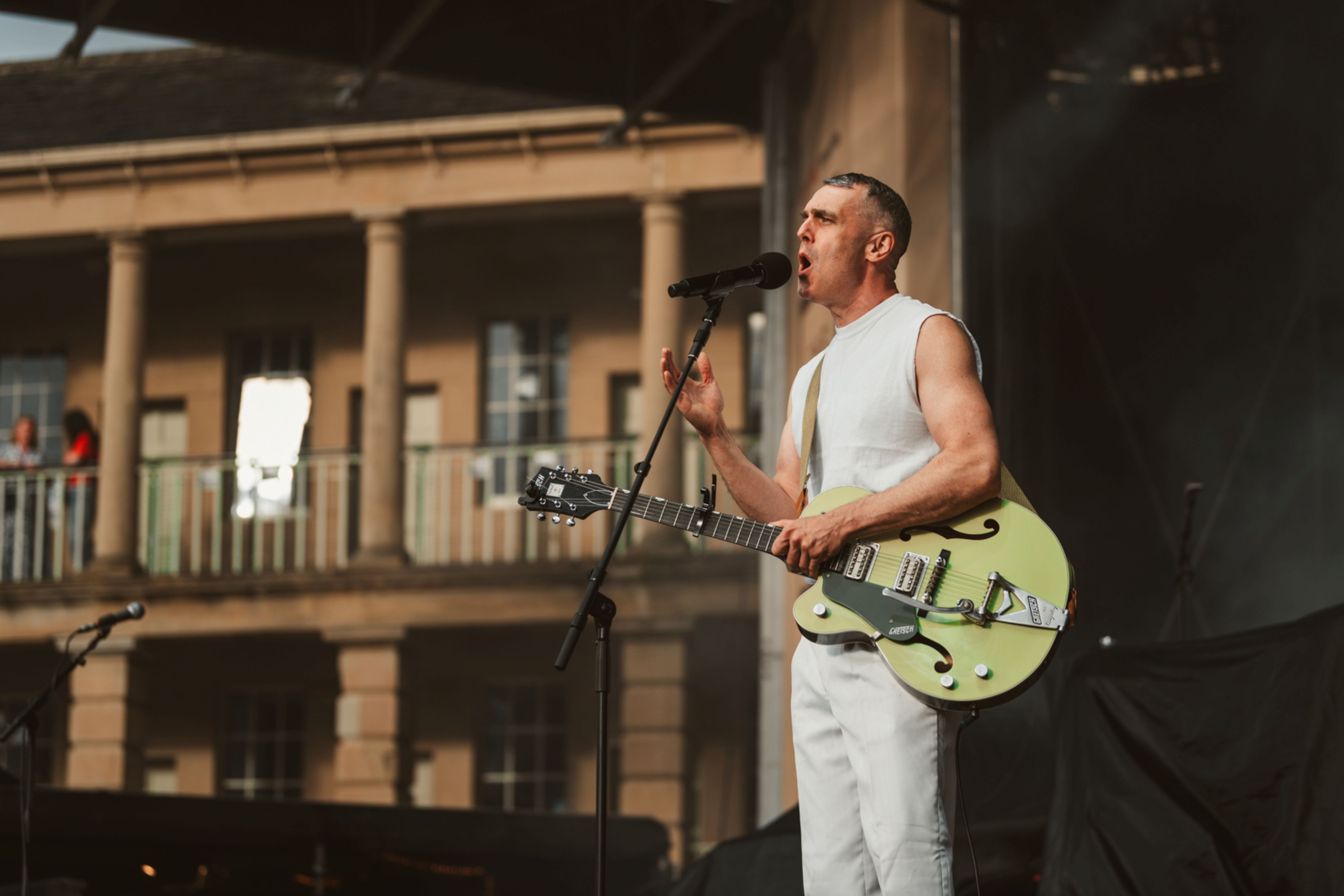 Musician in white performing with a green guitar on stage