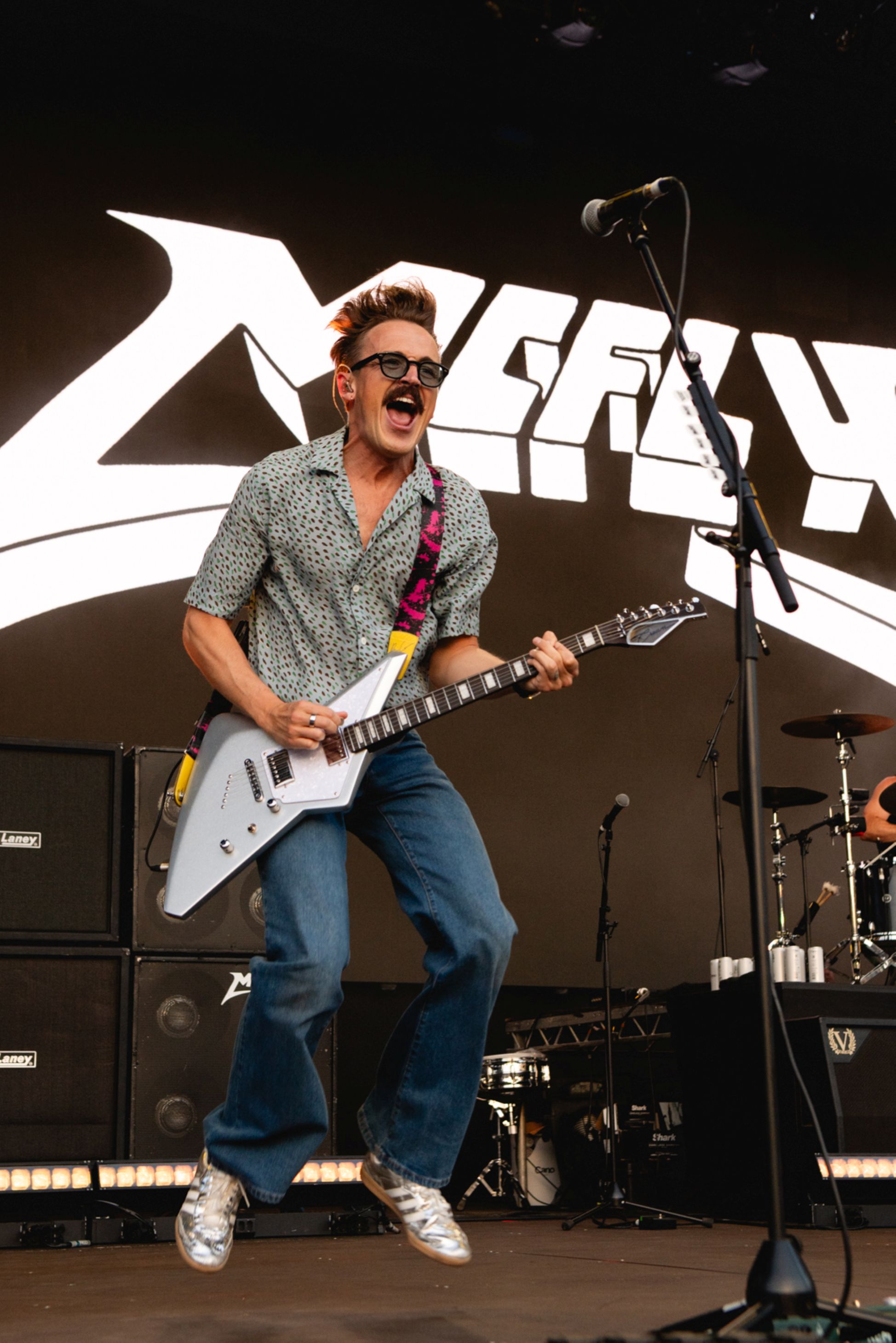 Guitarist in patterned shirt and jeans jumping on stage