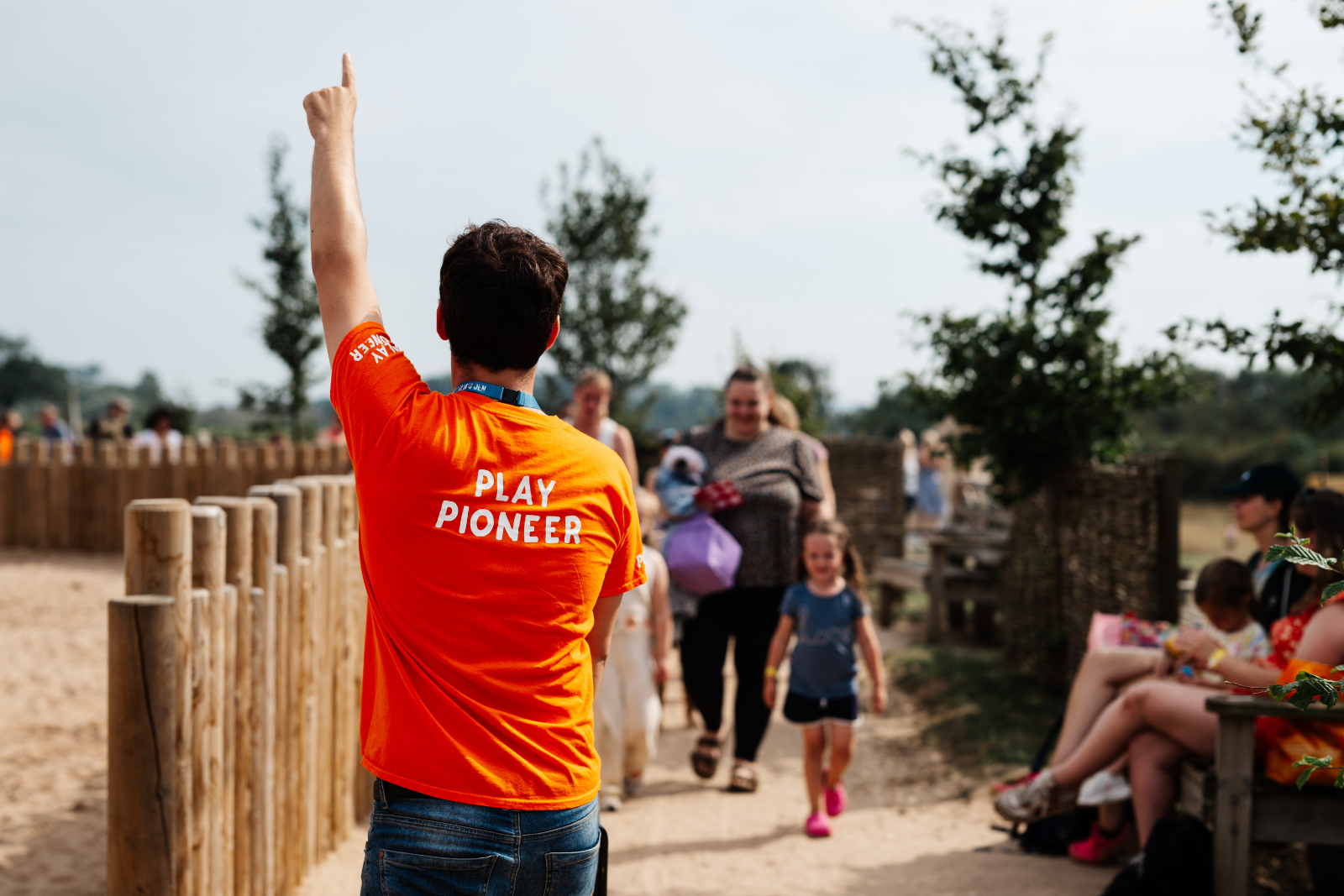Man in orange shirt leading children in outdoor play area