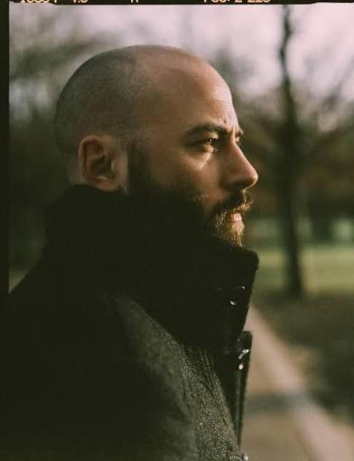 Man with a beard wearing a dark coat in a park setting