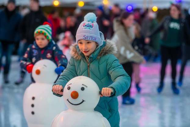 Children in winter coats skating with snowman figures on ice rink