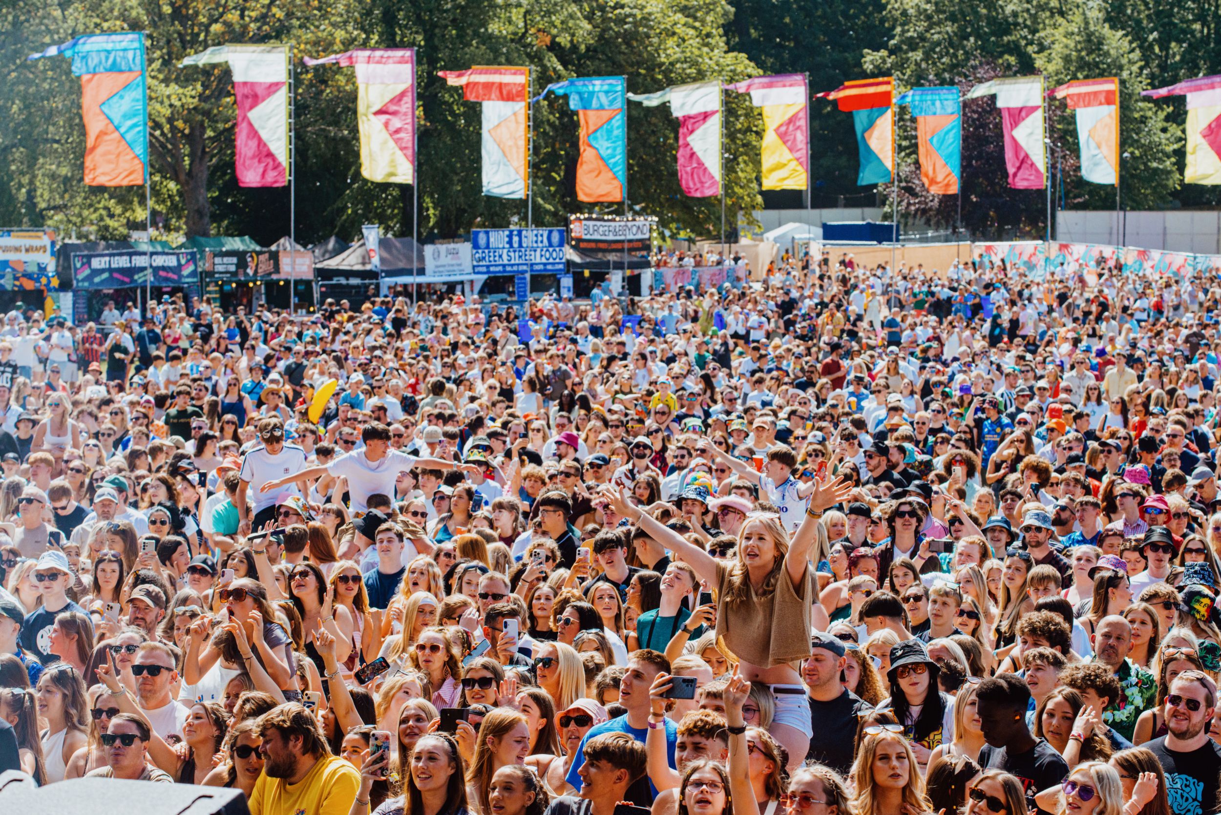 Large festival crowd with colourful flags under sunny sky