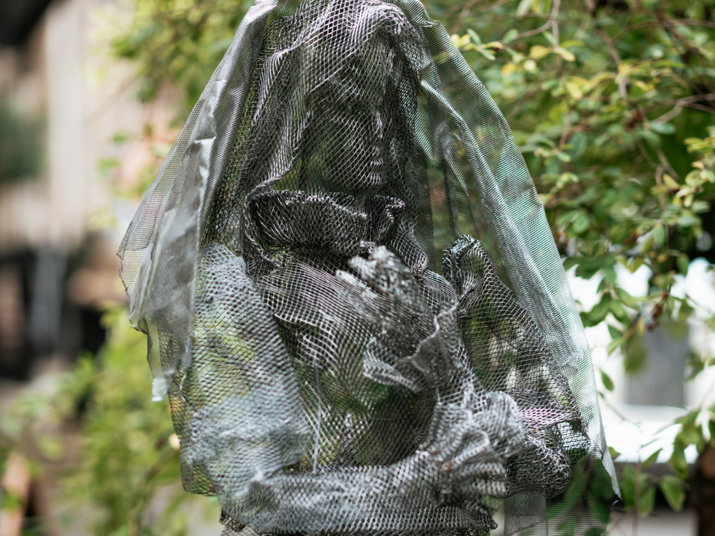 Intricate wire sculpture of a contemplative figure in garden