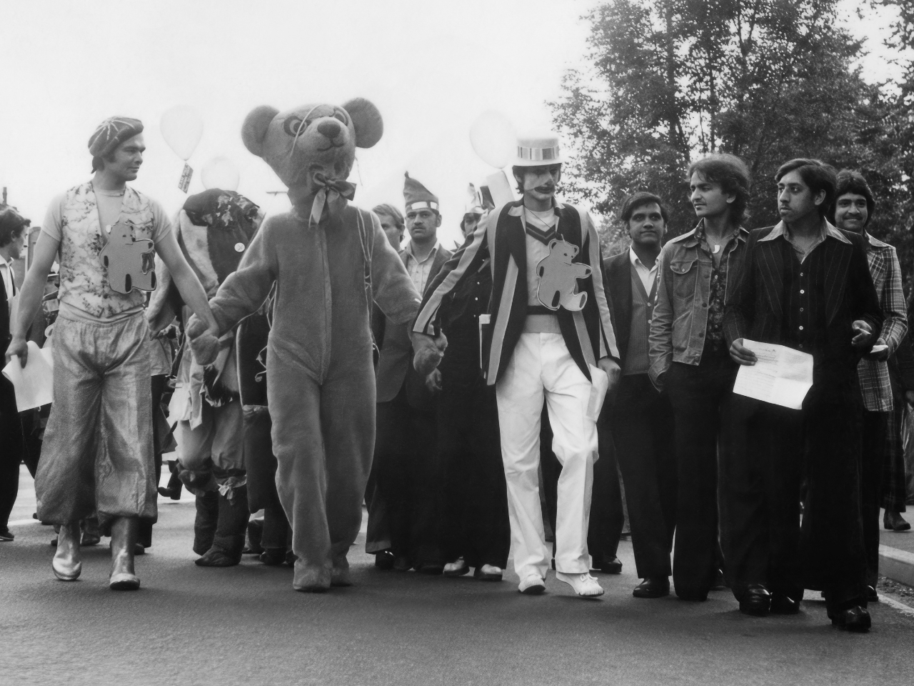 Parade with people in costumes and a bear mascot on a street