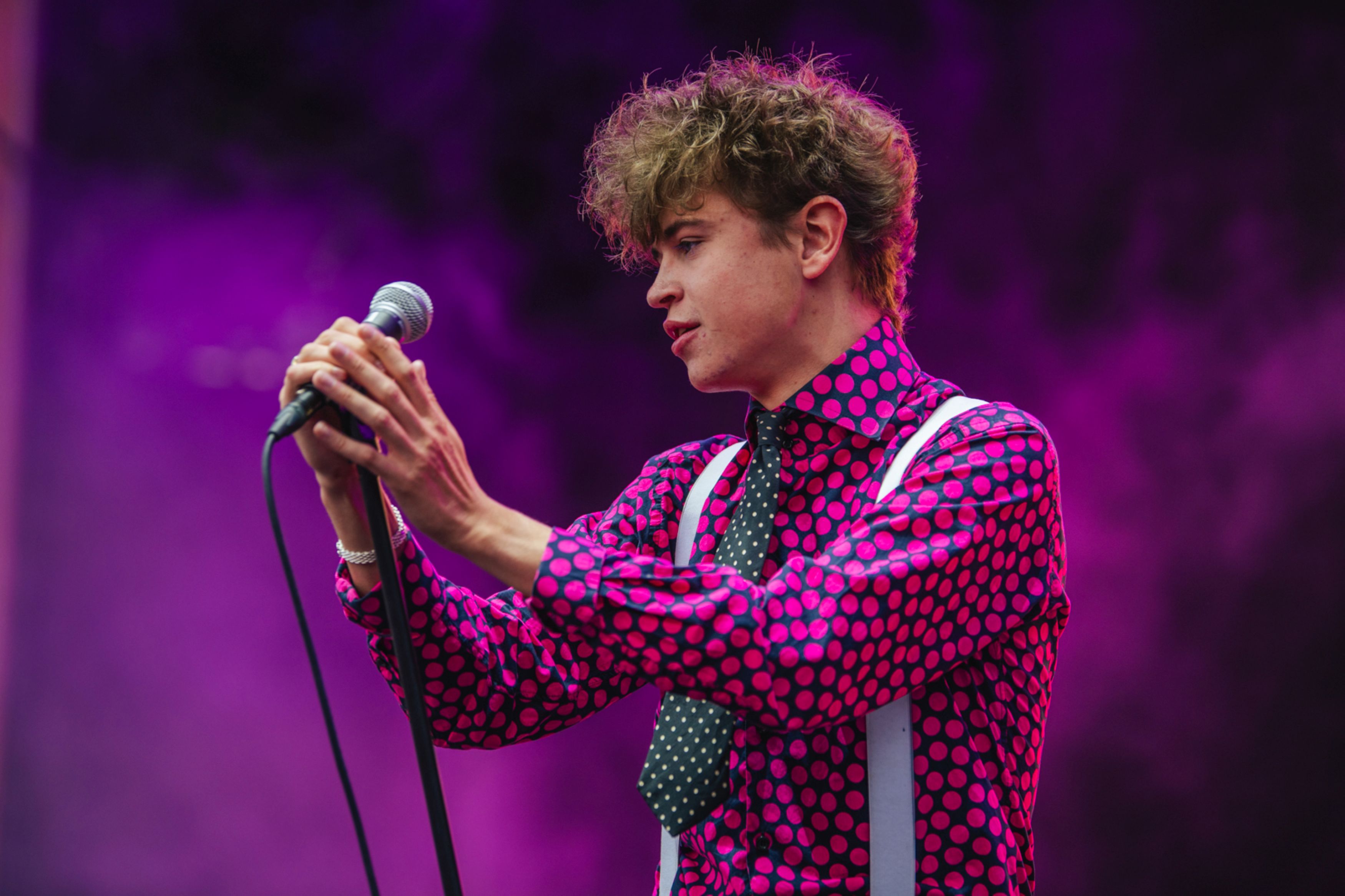 Singer in pink polka dot shirt performing on stage with purple lighting