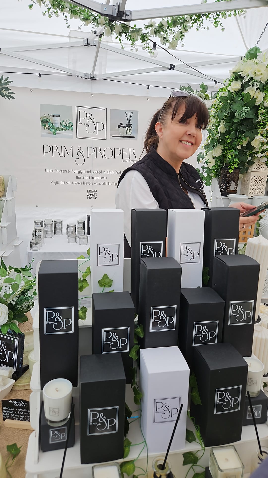 Smiling woman at a stall with candles and boxes at a market