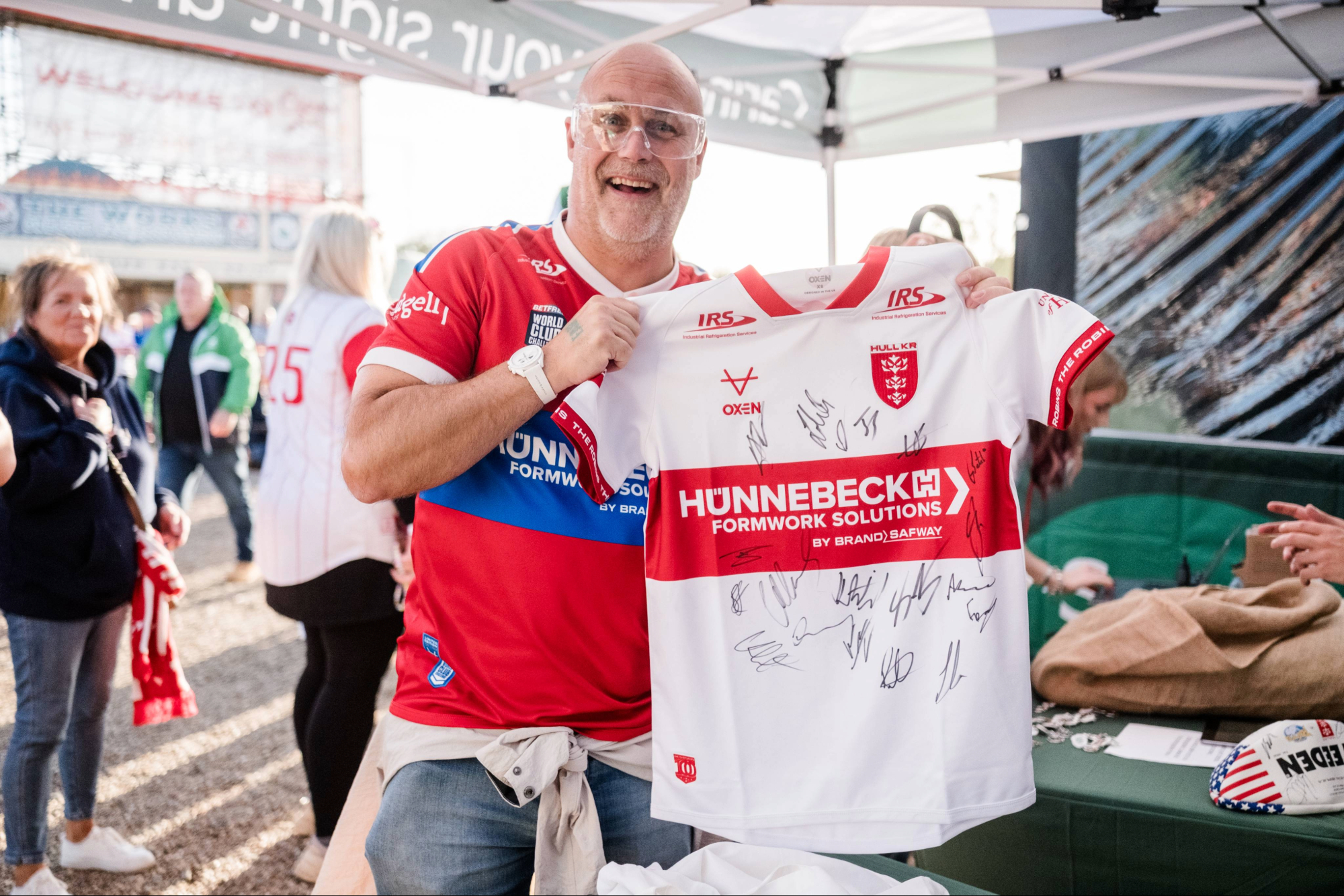 Man holding a signed rugby jersey at an outdoor event
