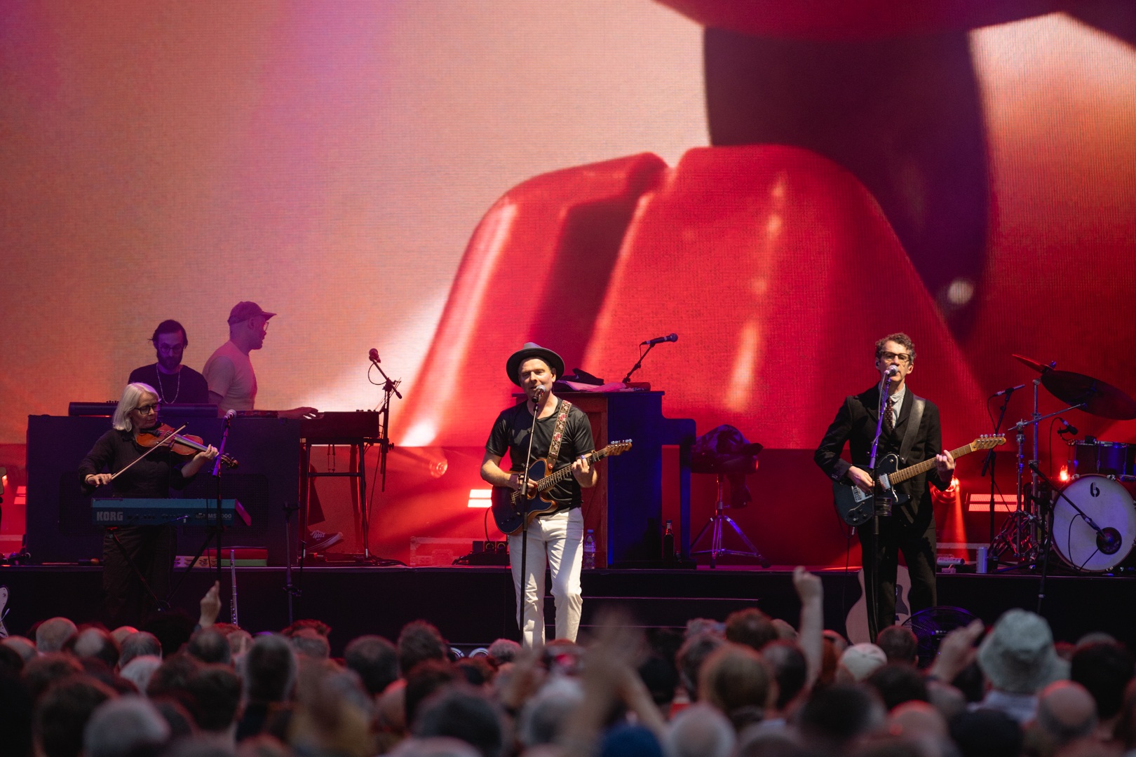 Band performing on stage with large screen and crowd in foreground
