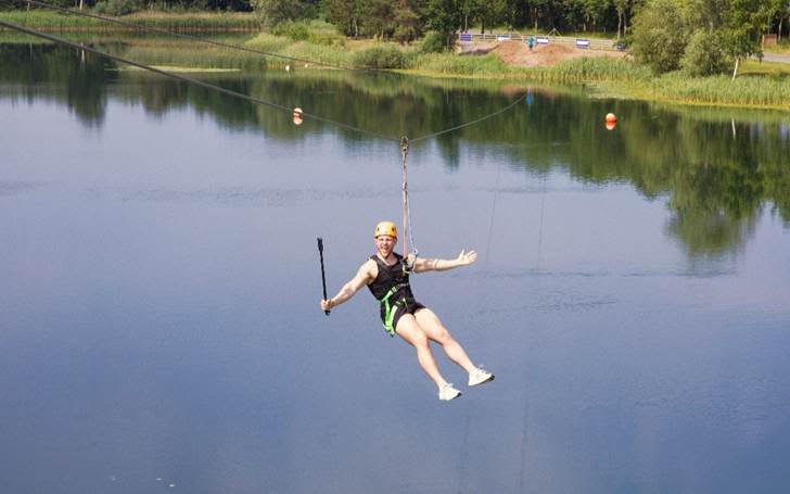 Person zip-lining over a tranquil lake surrounded by trees