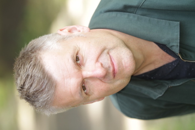 Man with short grey hair wearing a green jacket outdoors