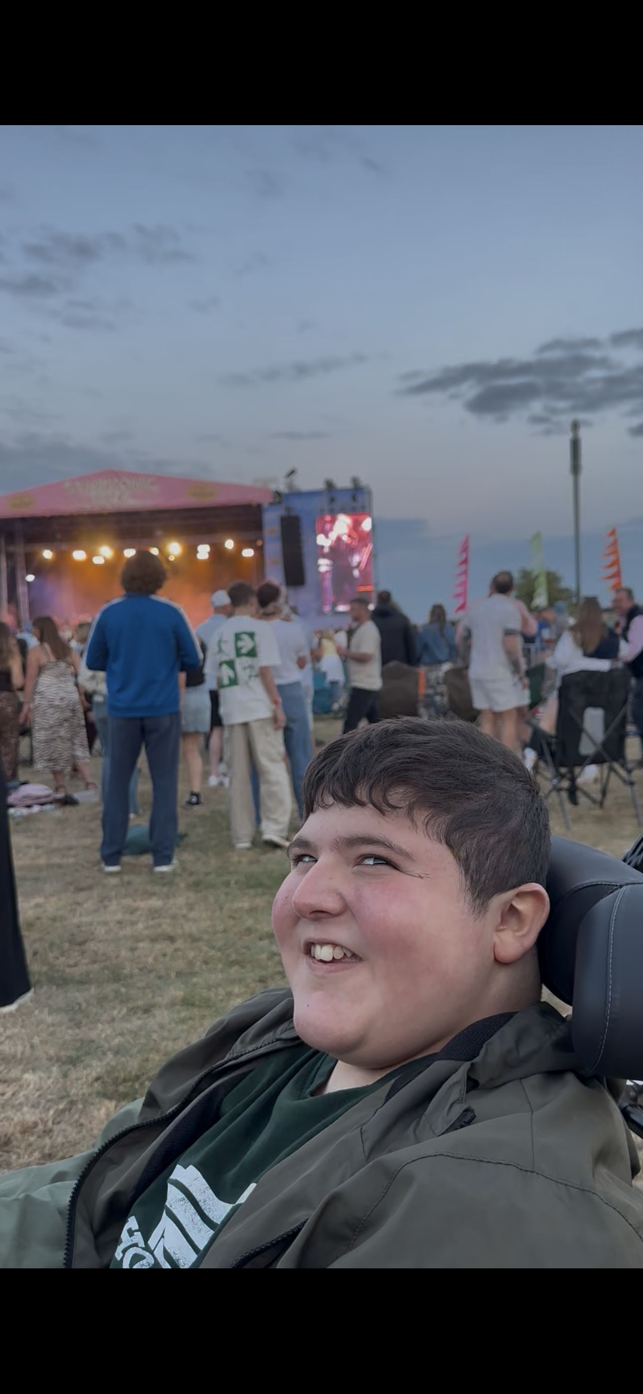 Smiling festival-goer in wheelchair with stage and crowd