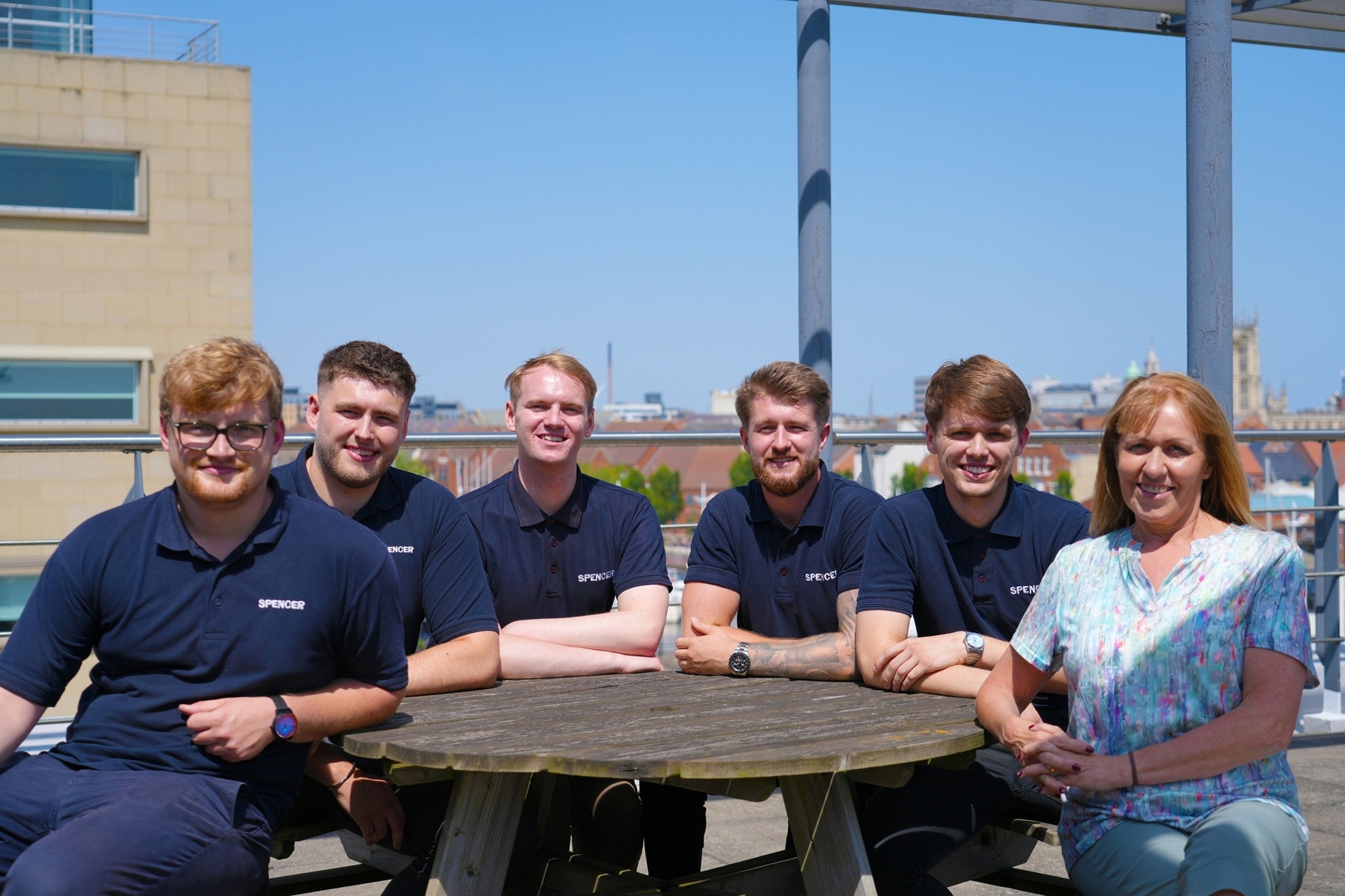 Group of people in blue shirts sitting at a wooden picnic table