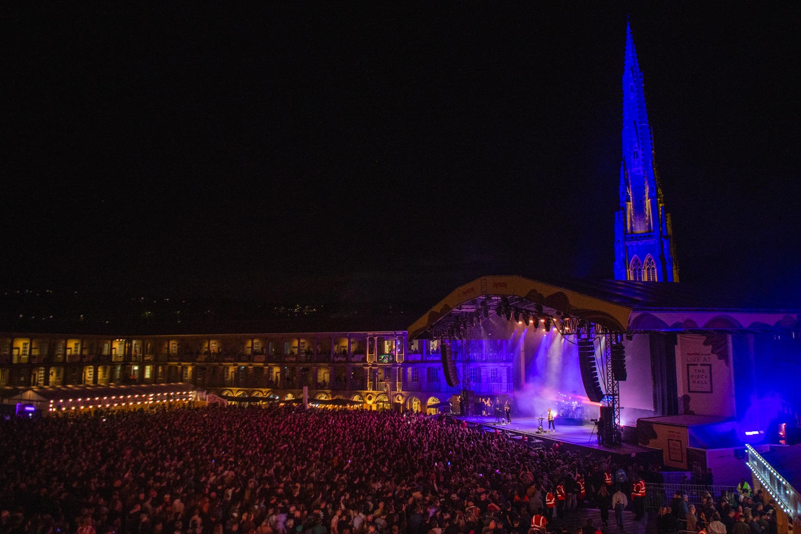 Night concert at Halifax Piece Hall with illuminated church spire