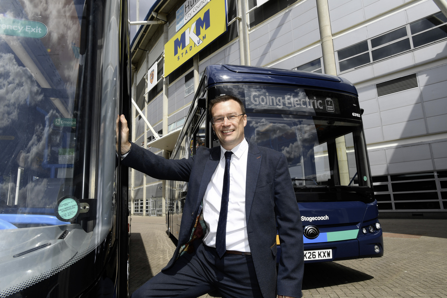 Man in suit standing beside electric bus outside stadium
