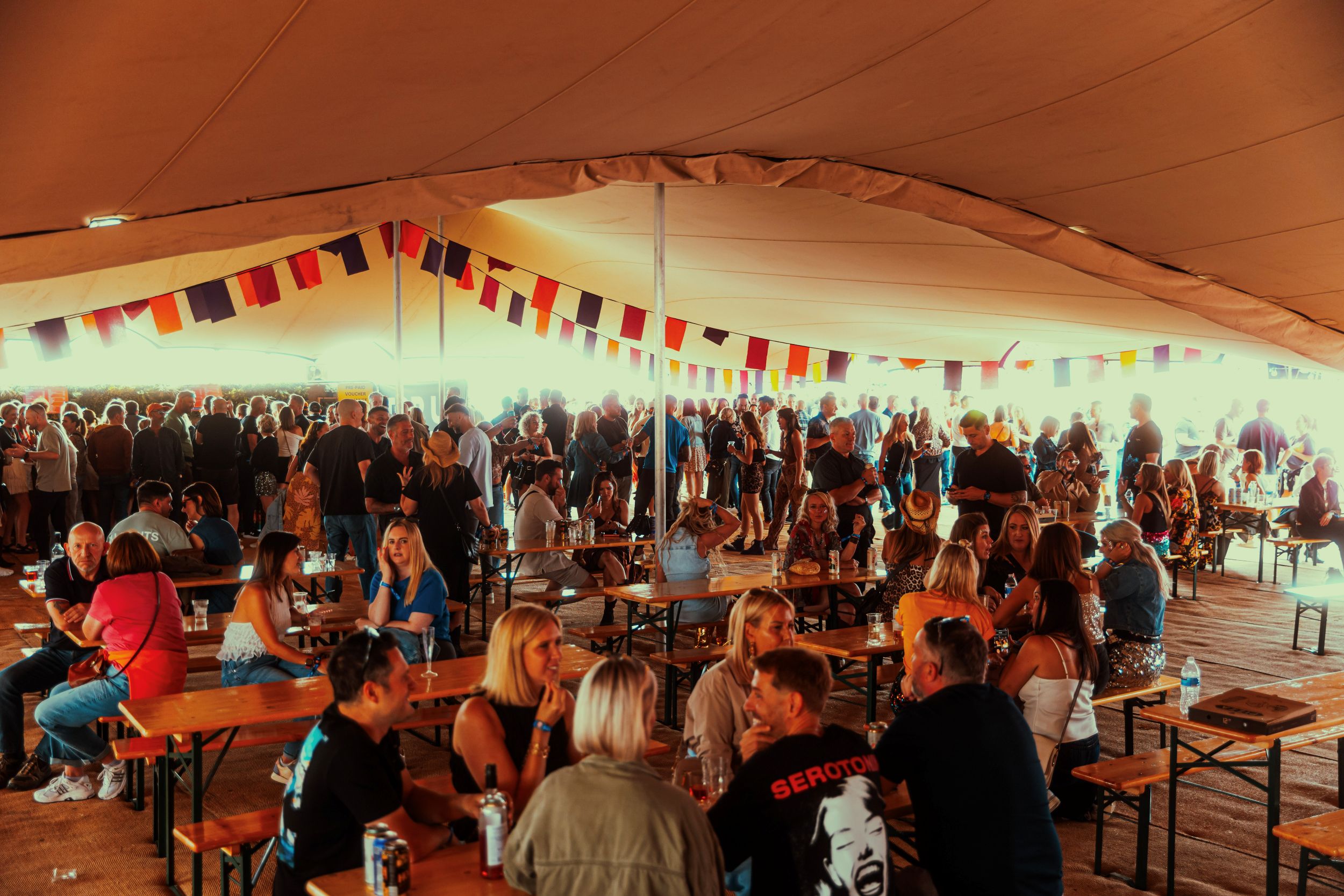 Crowded festival tent with colorful flags and wooden tables