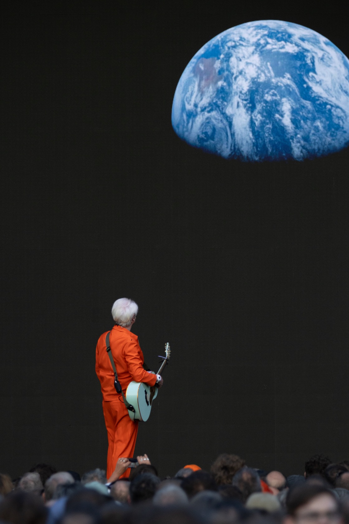 Person in orange suit with guitar gazing at earth on screen