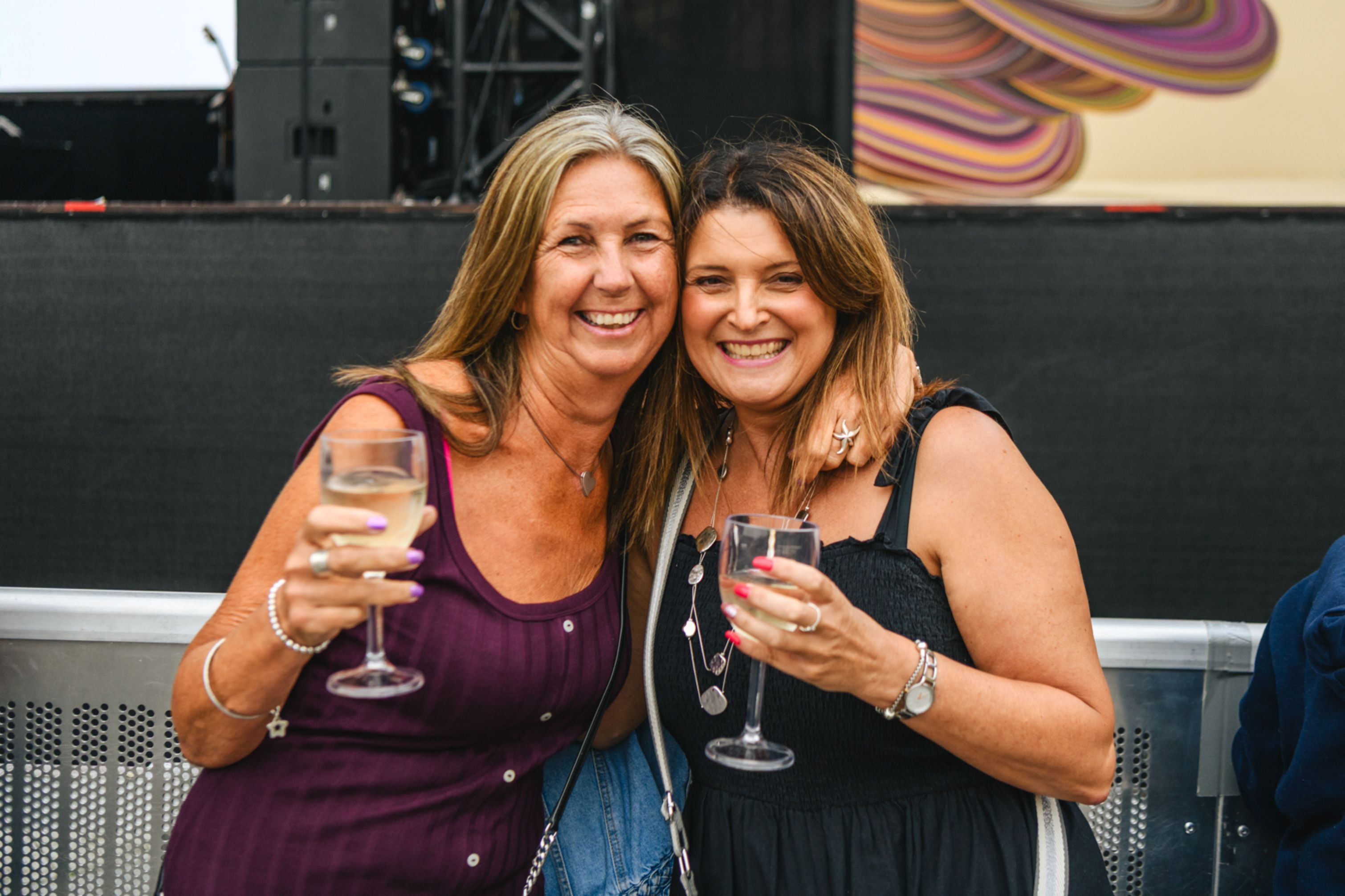 Two women smiling and holding wine glasses at an outdoor event