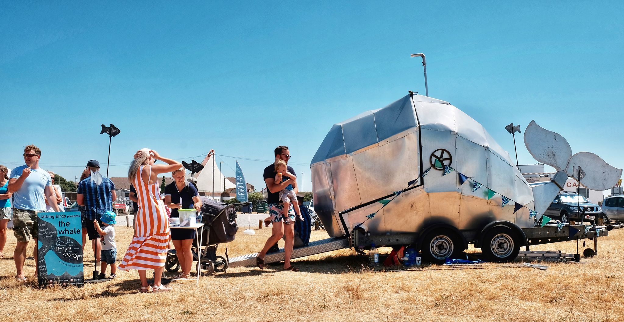 People gathered around a silver caravan with whale tail artwork
