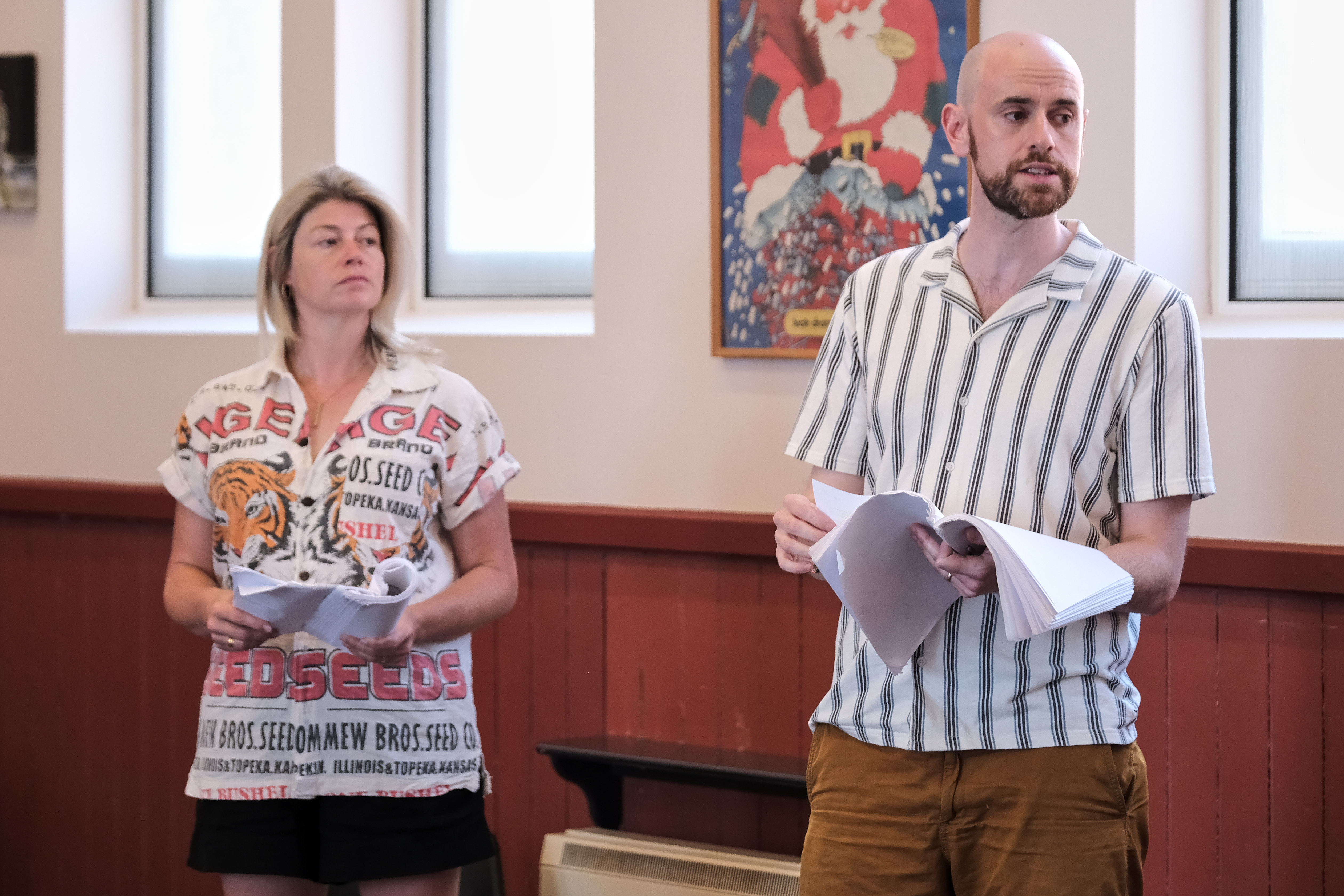 Two people in summer shirts holding scripts in a red room