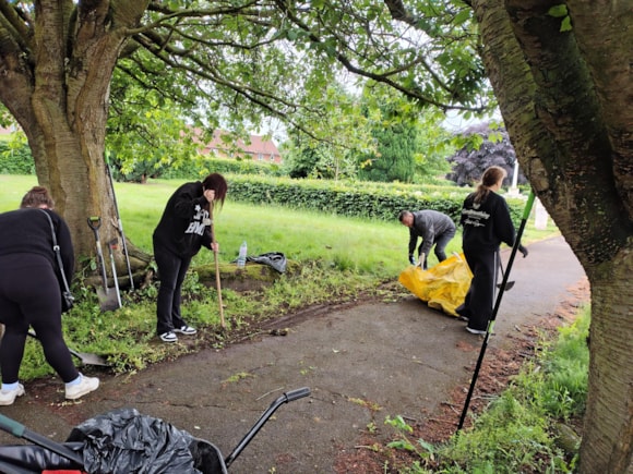 Volunteers cleaning a park path surrounded by trees