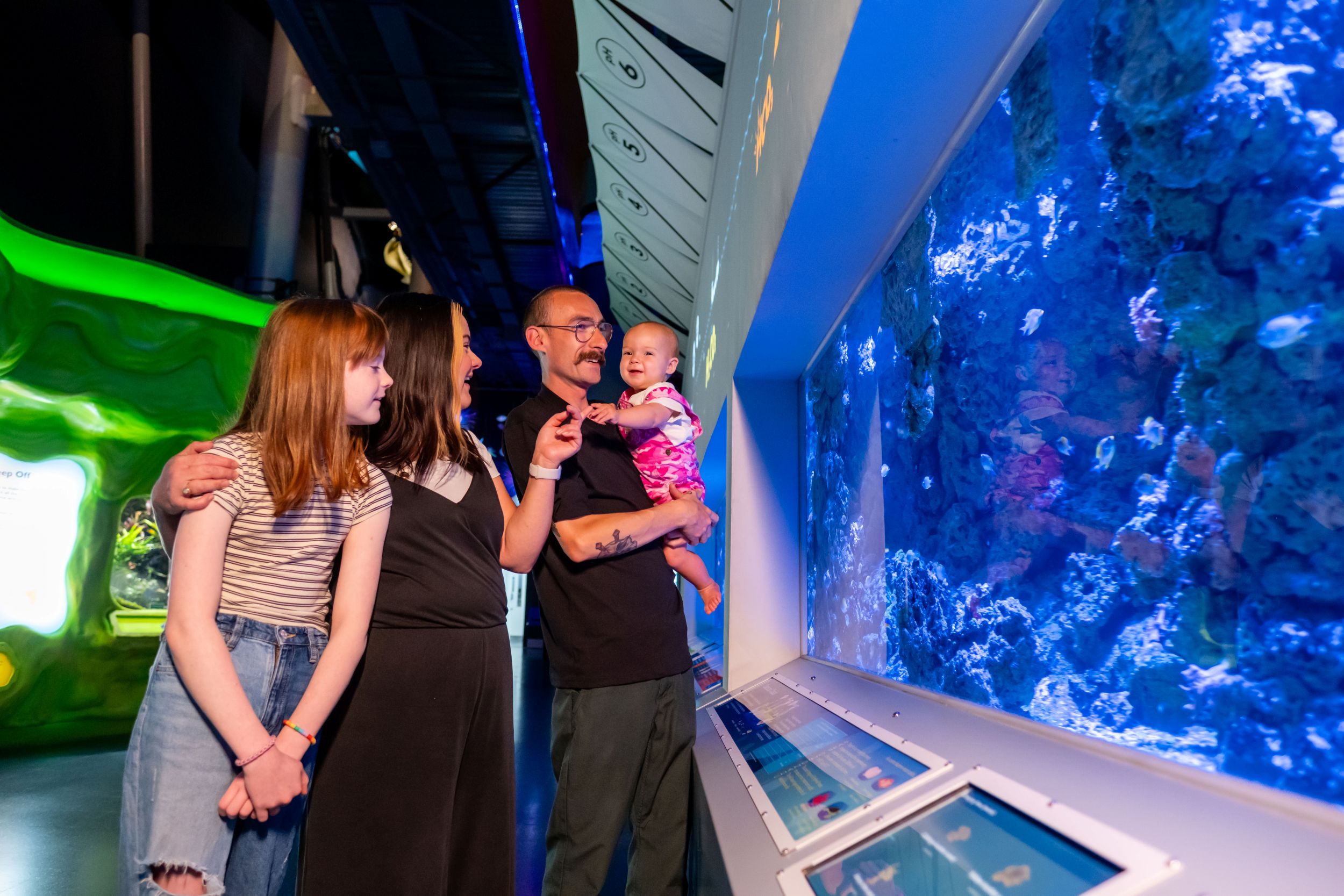 Family observing vibrant coral reef display at aquarium