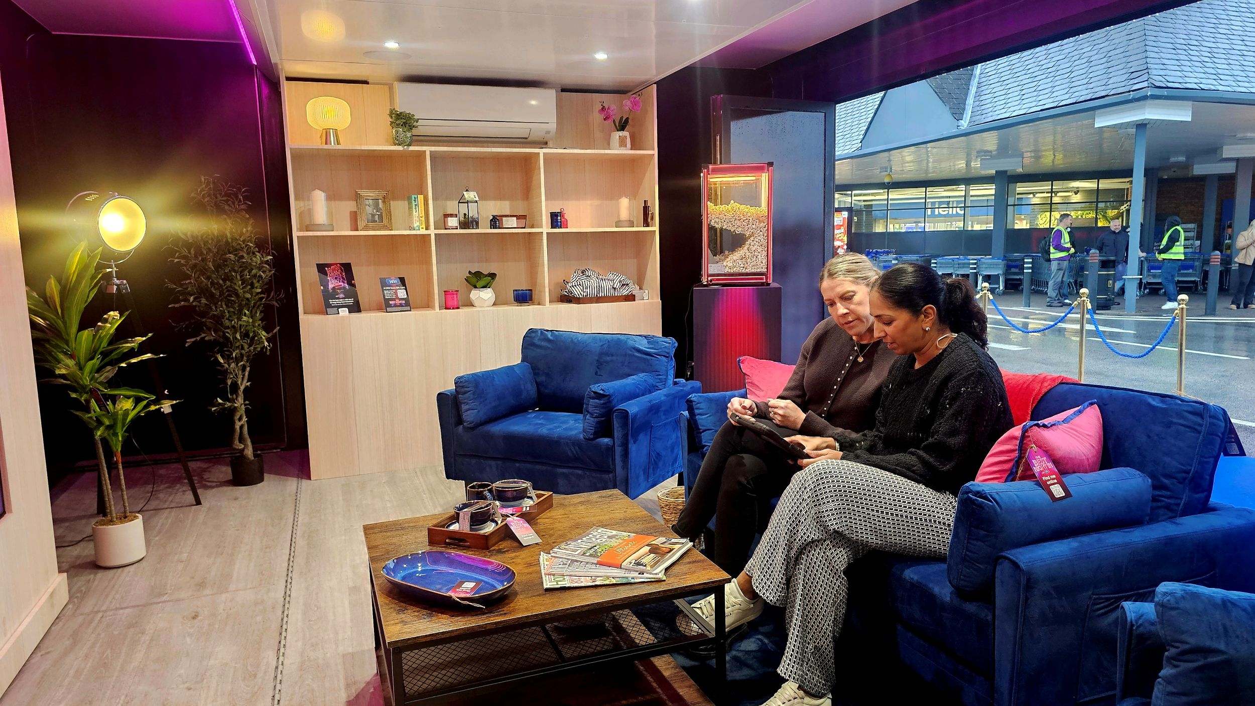 Two people on blue sofas in a modern lounge with shelves and plants