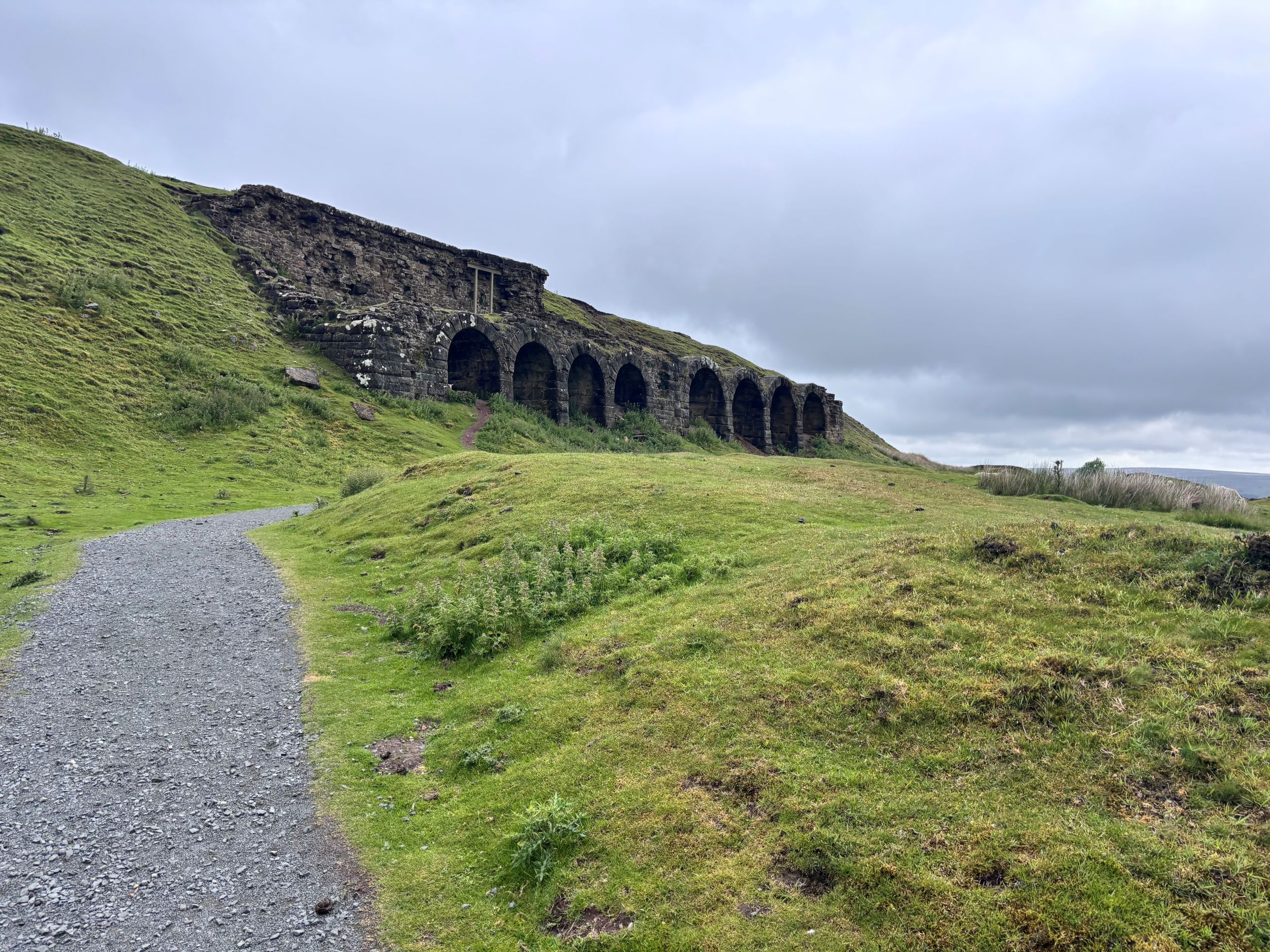 Historic stone viaduct arches on grassy hillside under cloudy sky