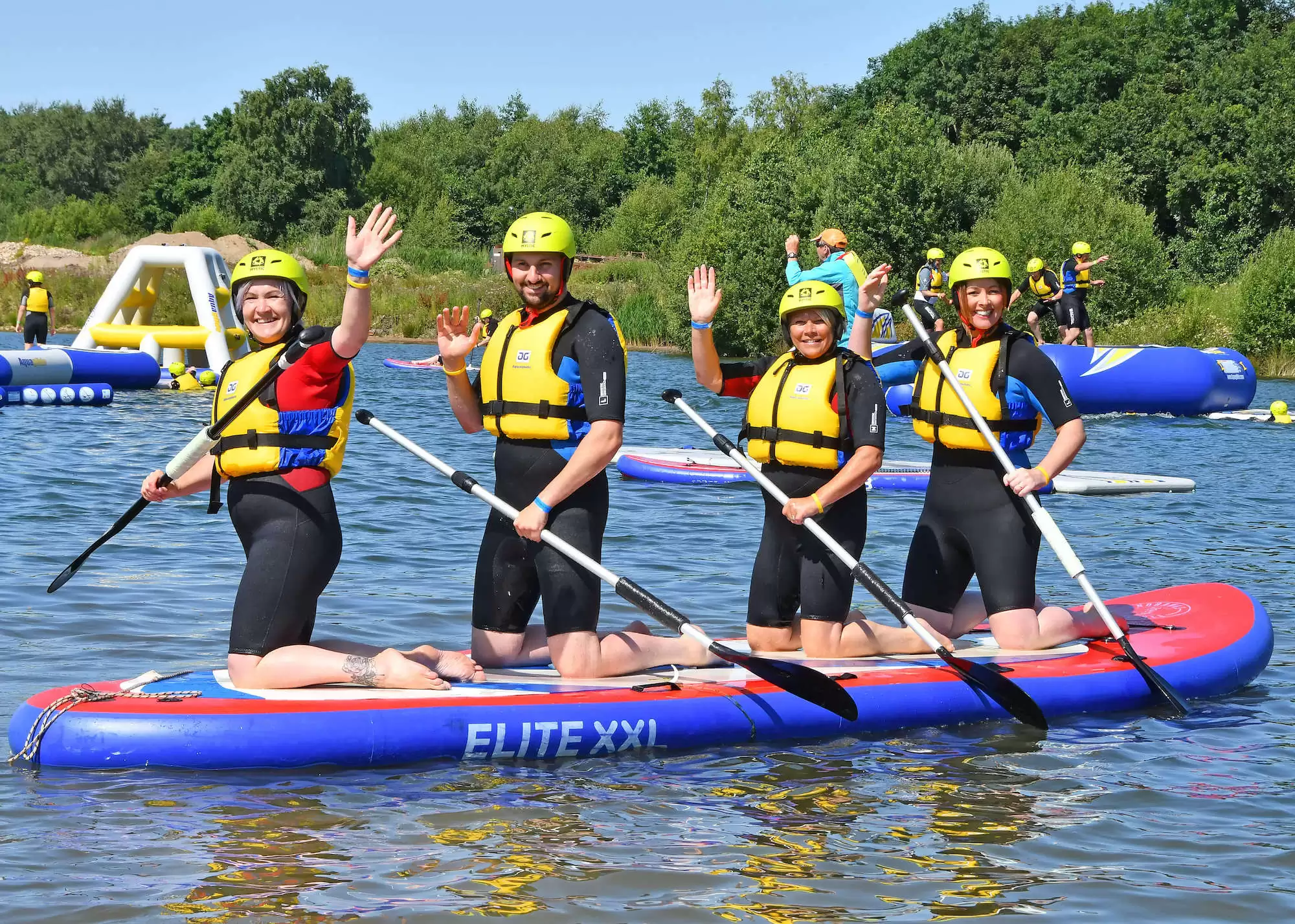 Group paddleboarding on lake with life jackets and helmets