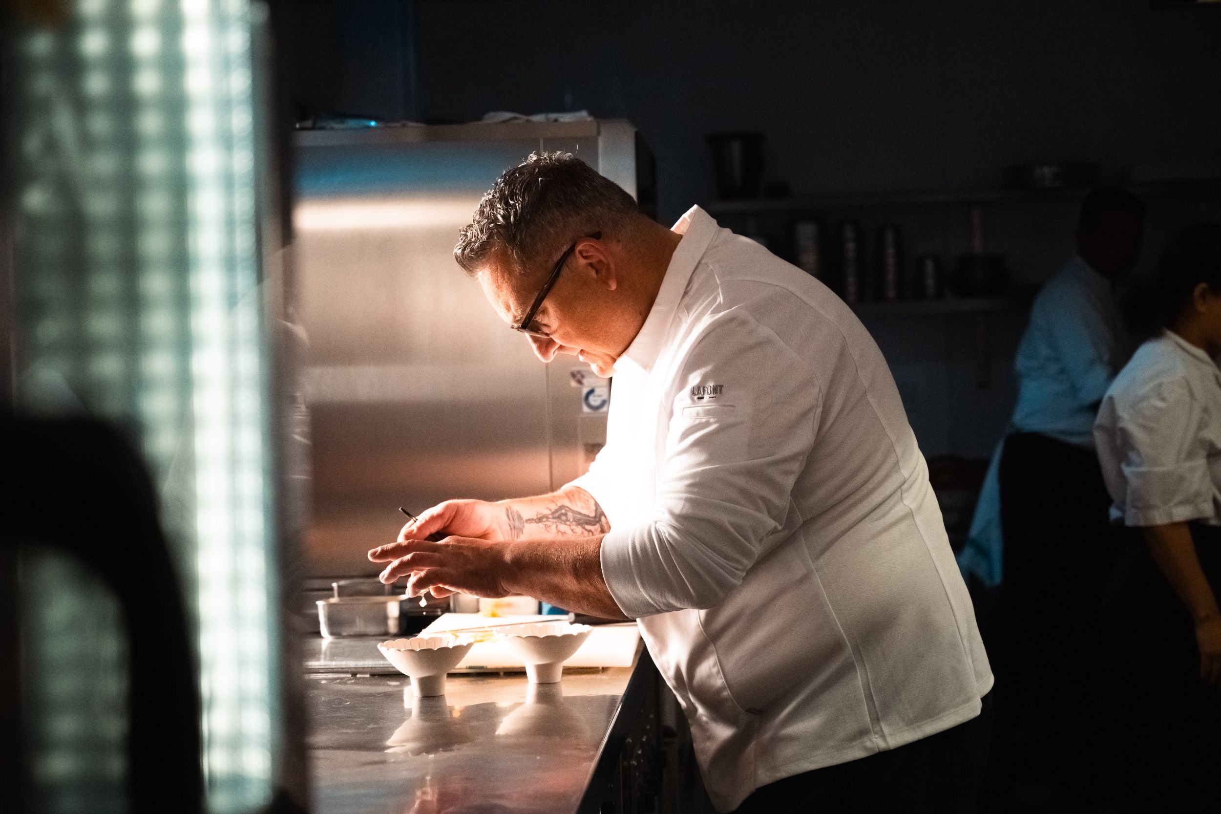 Chef in white uniform plating gourmet dish in kitchen