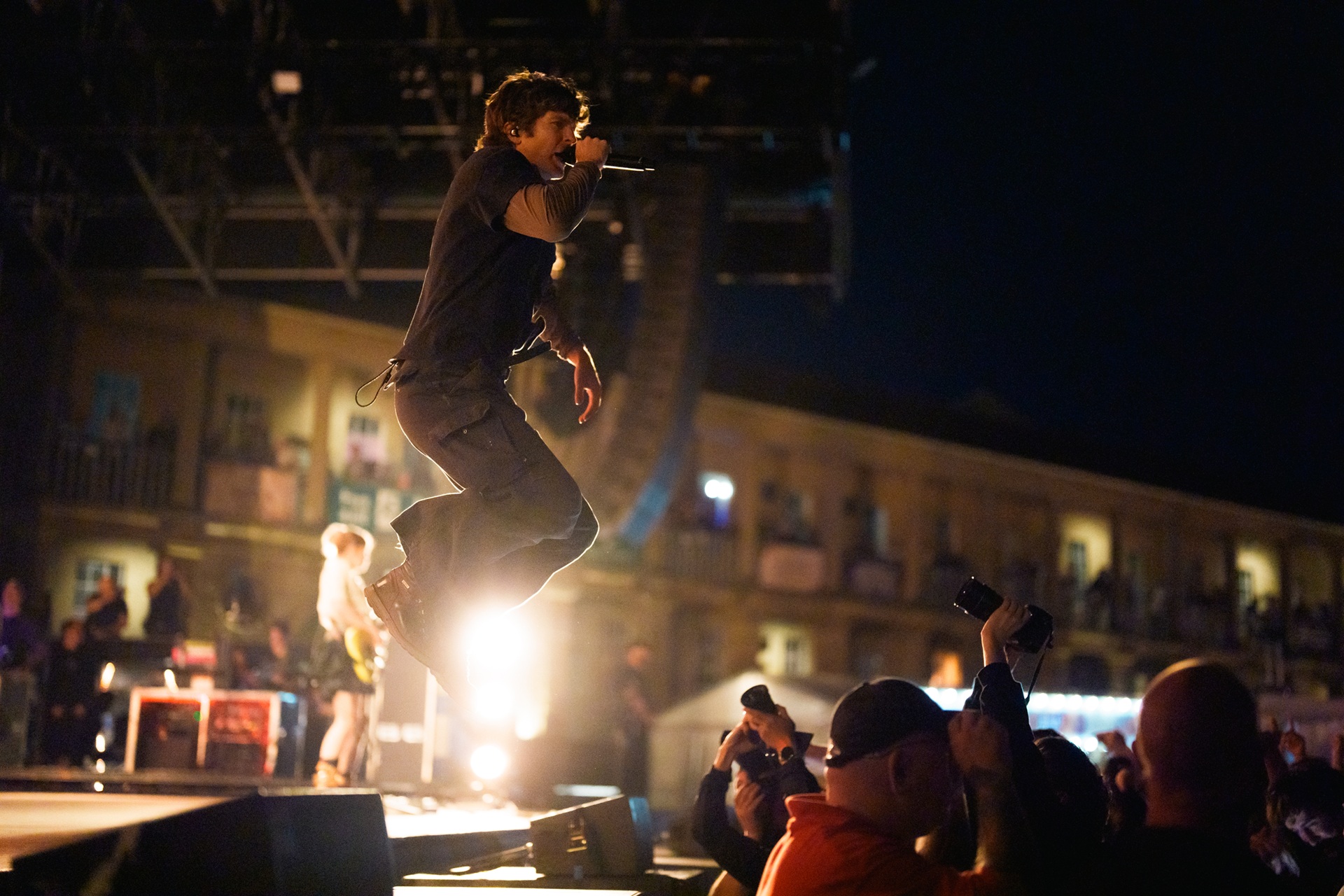 Musician mid-air on stage with crowd and historic building