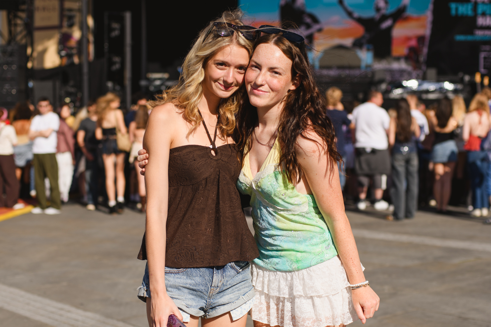 Two women smiling at an outdoor music festival in summer attire