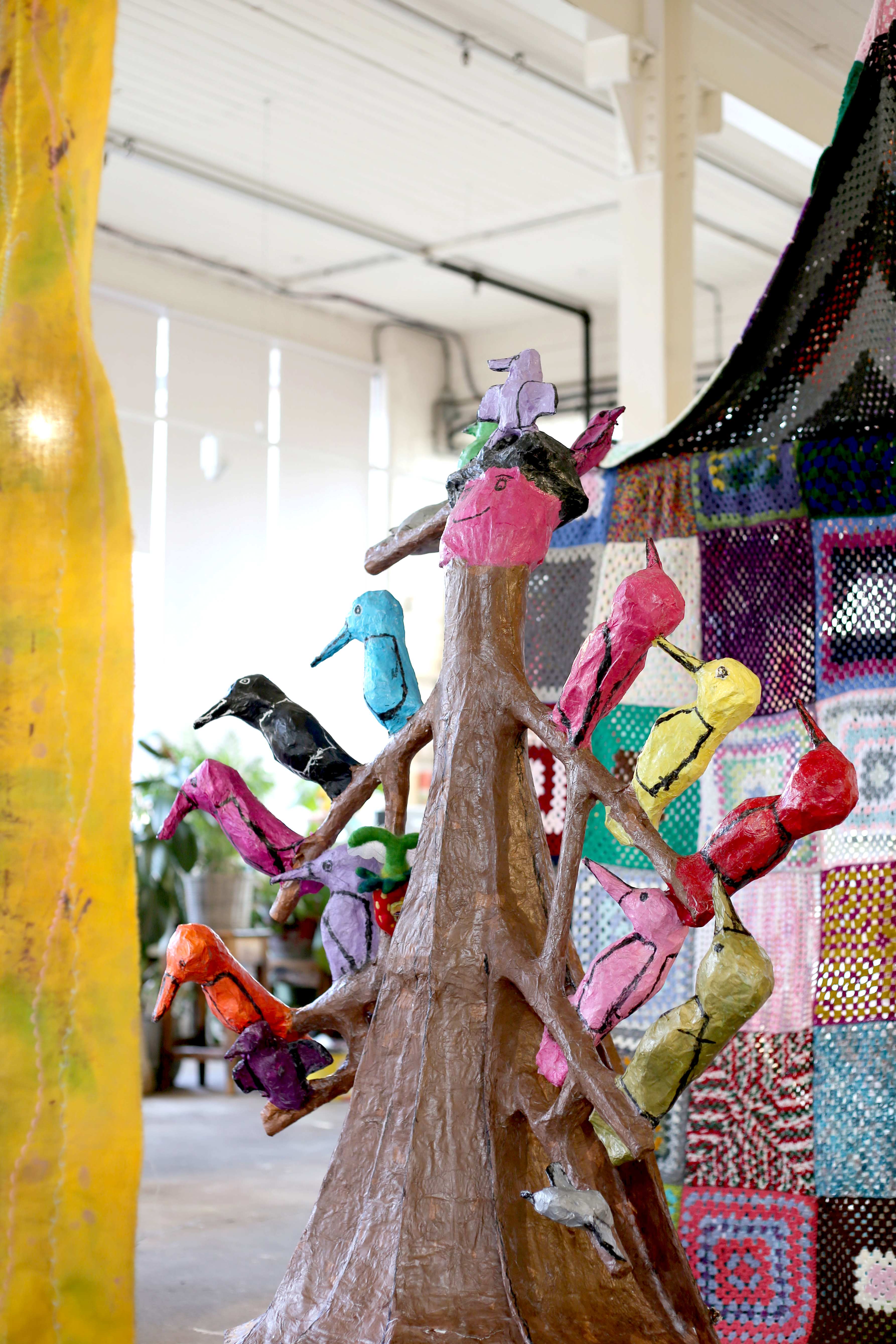 Colorful bird sculptures on a tree inside an art gallery