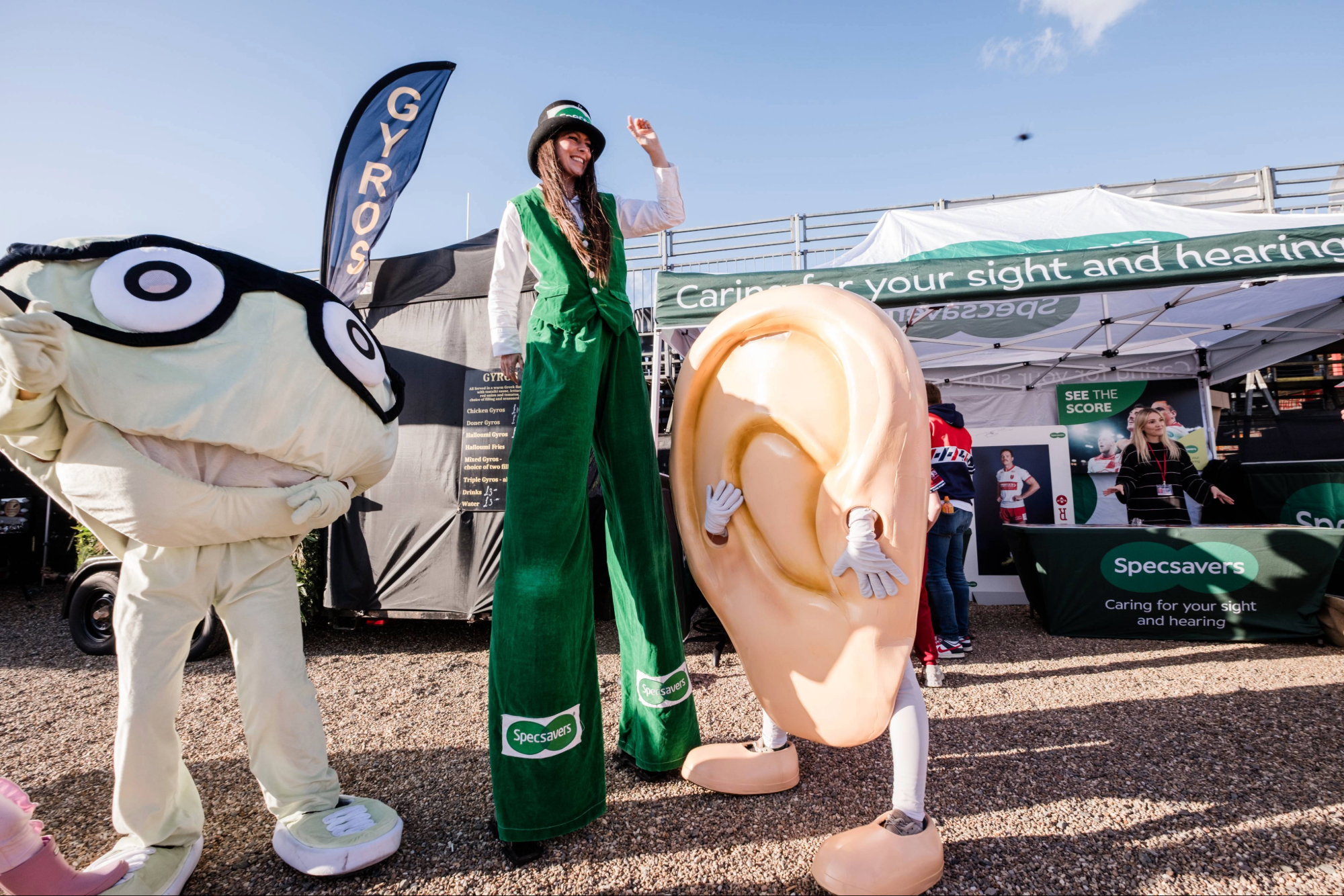 Street performer on stilts with ear and glasses mascots at festival