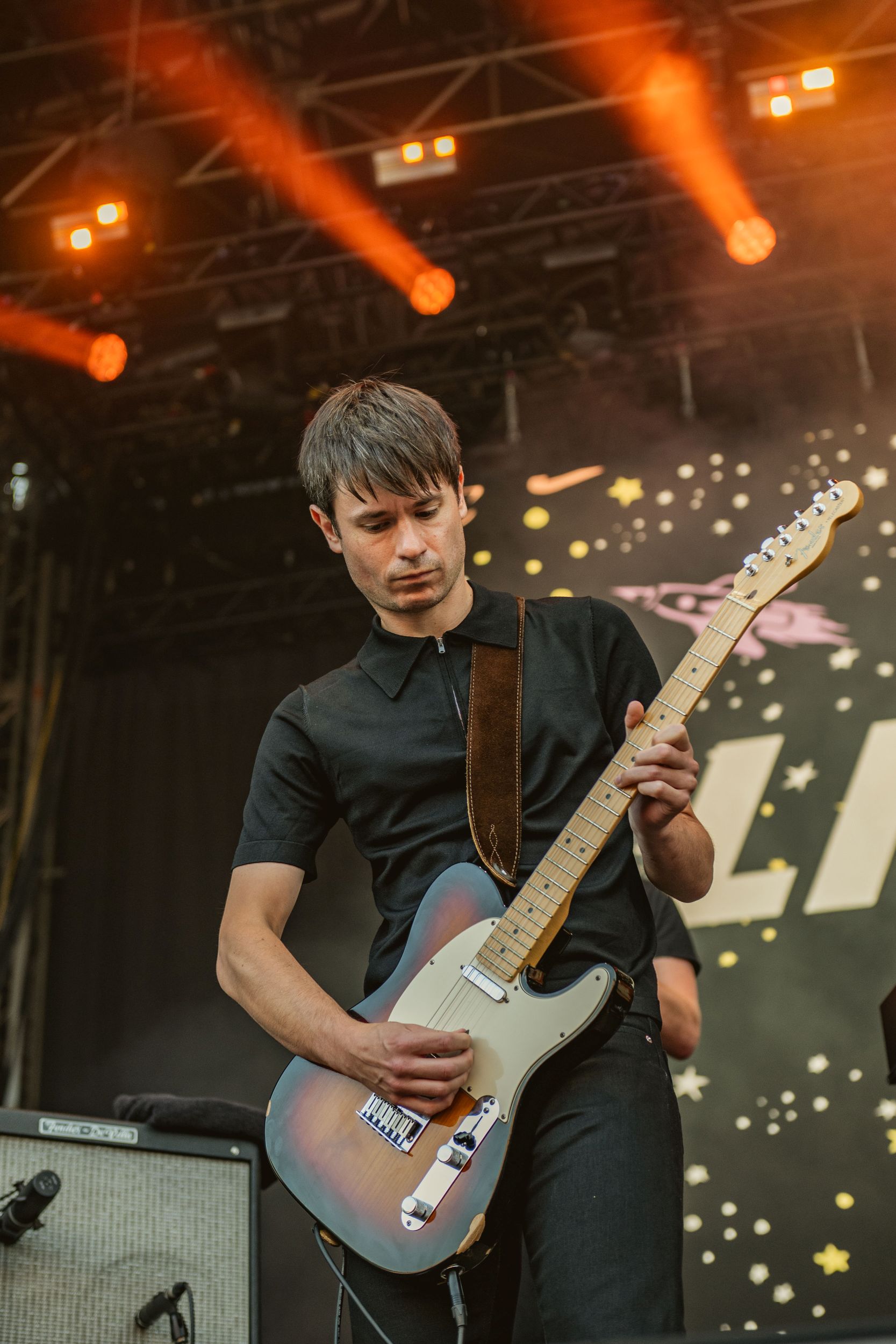 Guitarist in black playing on stage with starry backdrop