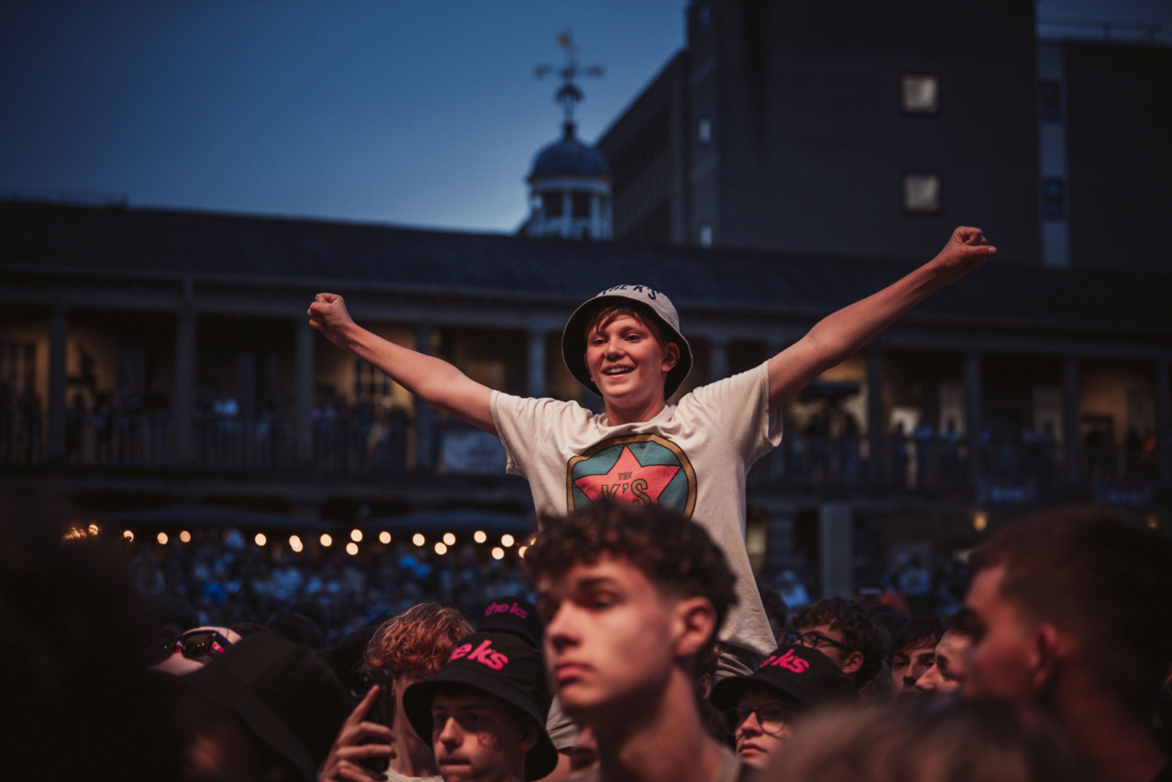 Joyful crowd at outdoor concert, person raised on shoulders