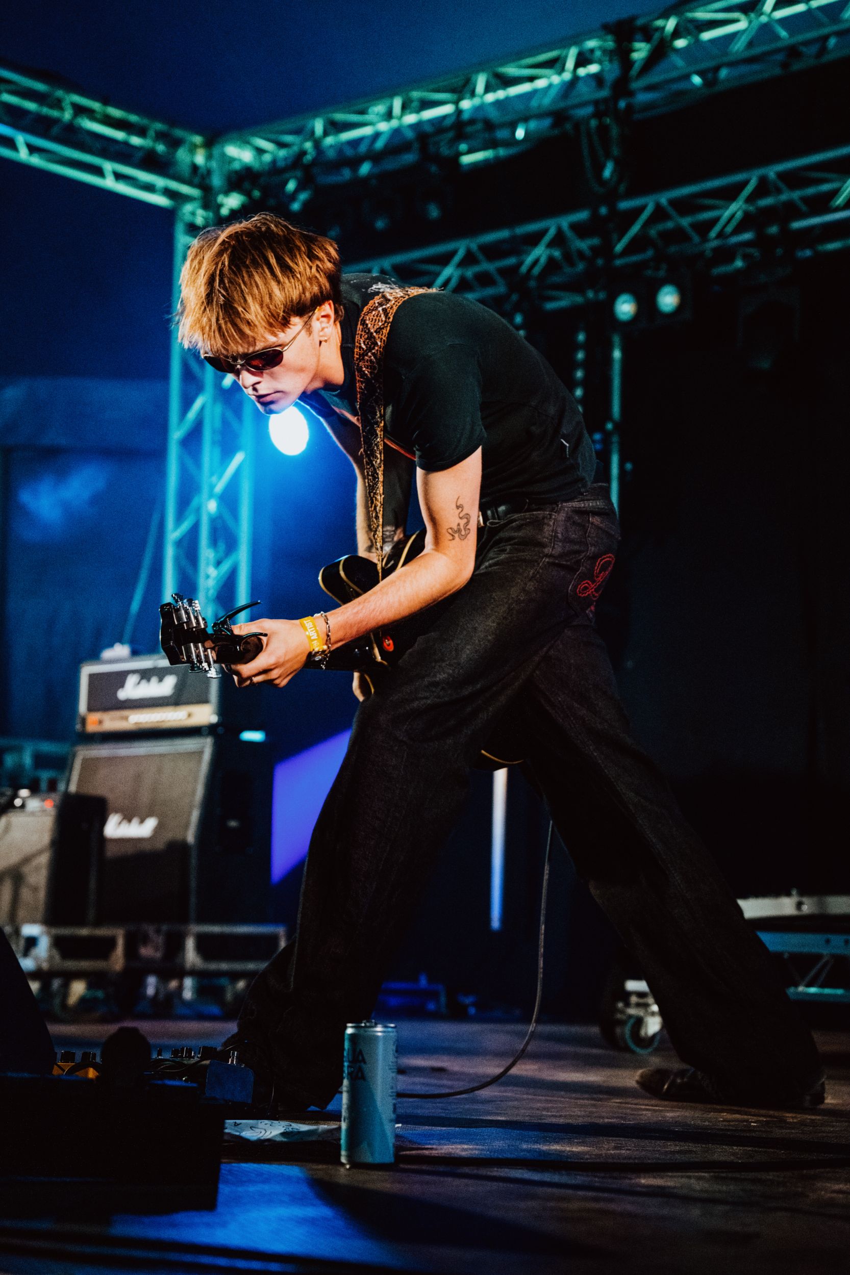 Musician in sunglasses playing guitar on stage with blue lights