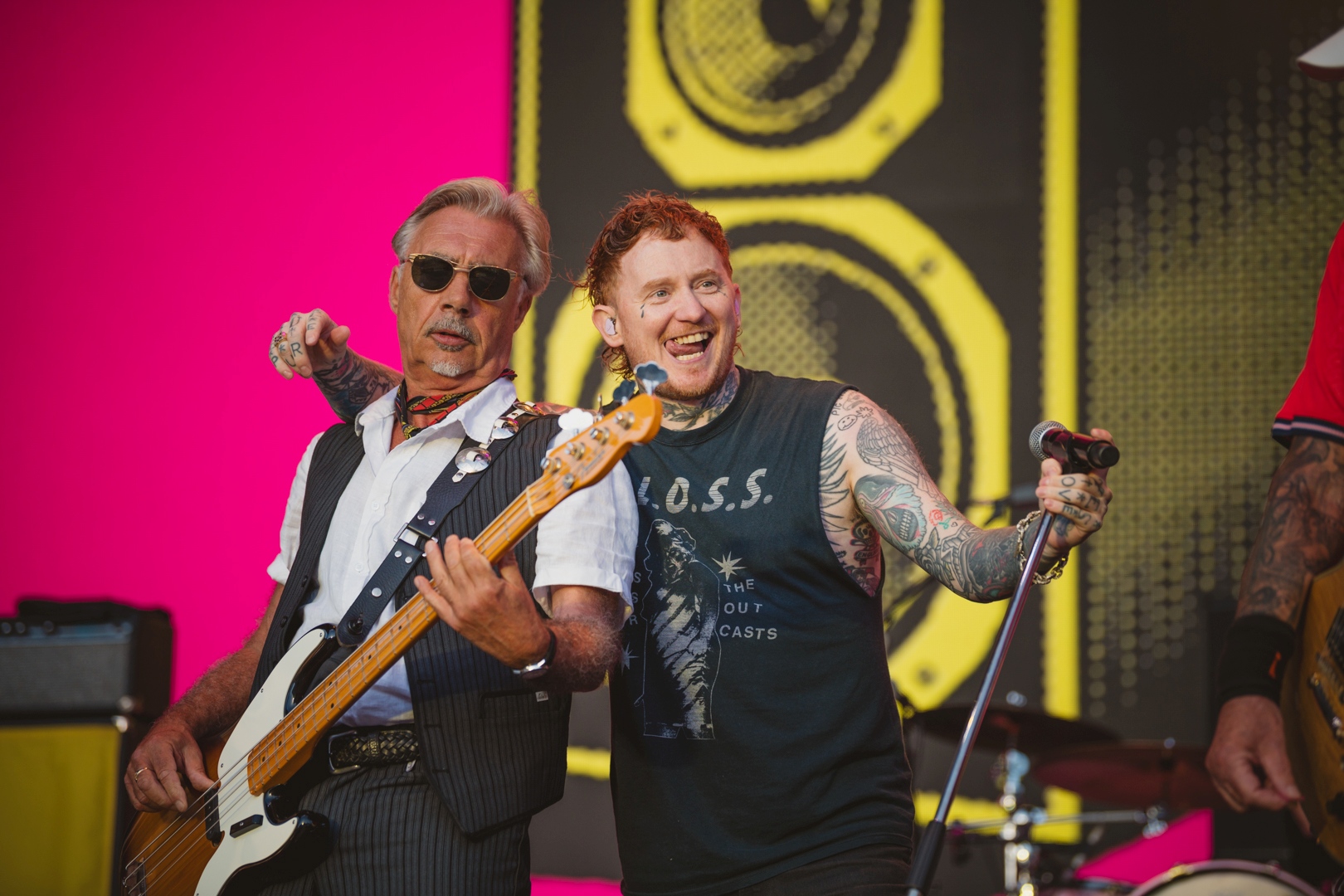 Two musicians on stage, one with a bass guitar, vibrant background